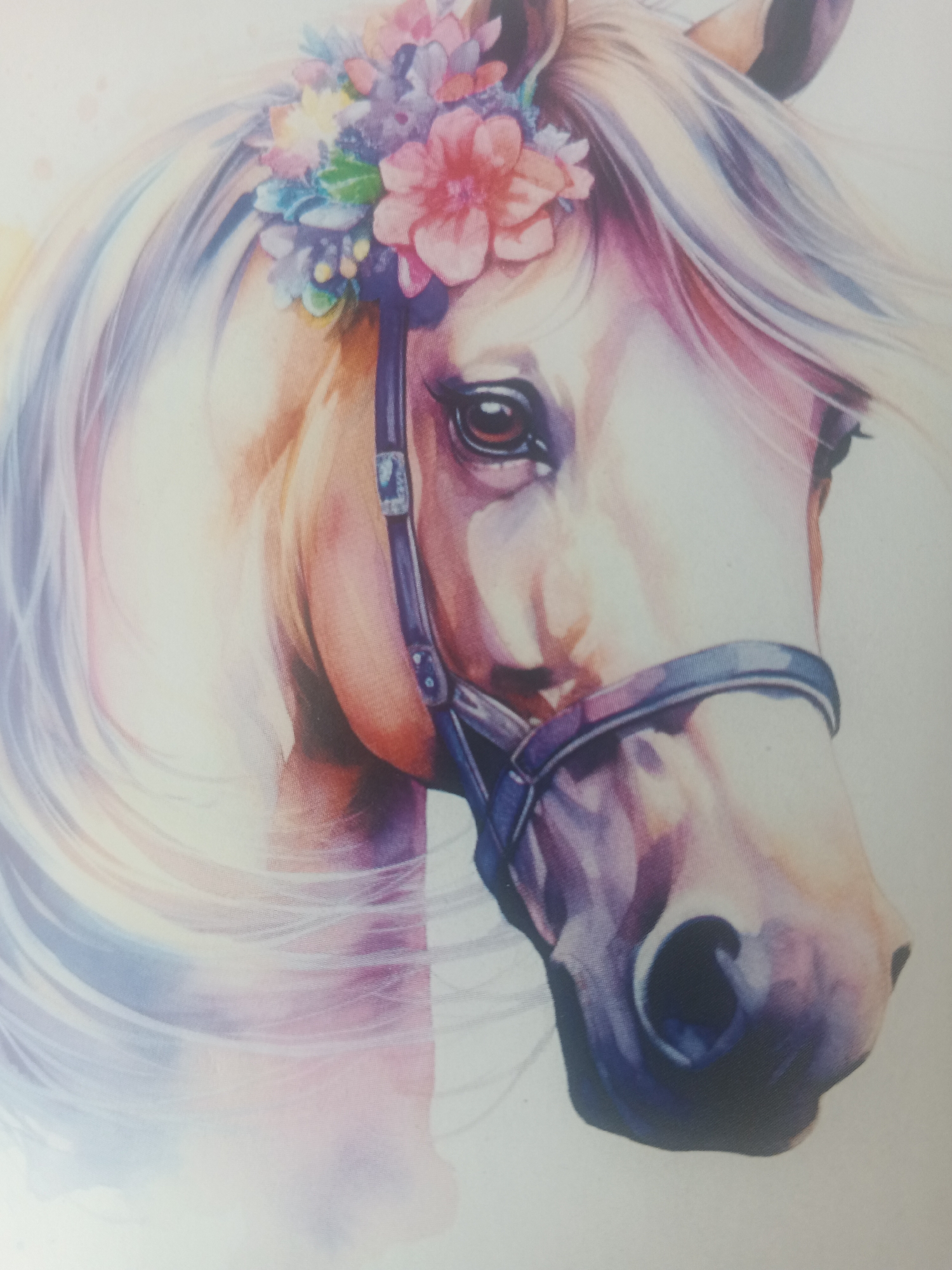 This is a close-up watercolor painting of a horse's head, adorned with a floral crown. The horse has light-colored mane and tail, with touches of pink, purple, and blue watercolor accents. It is wearing a dark bridle. The background is plain white, suggesting the image is a print or a digital reproduction. There is no indication of any specific location in Biysk, Russia.