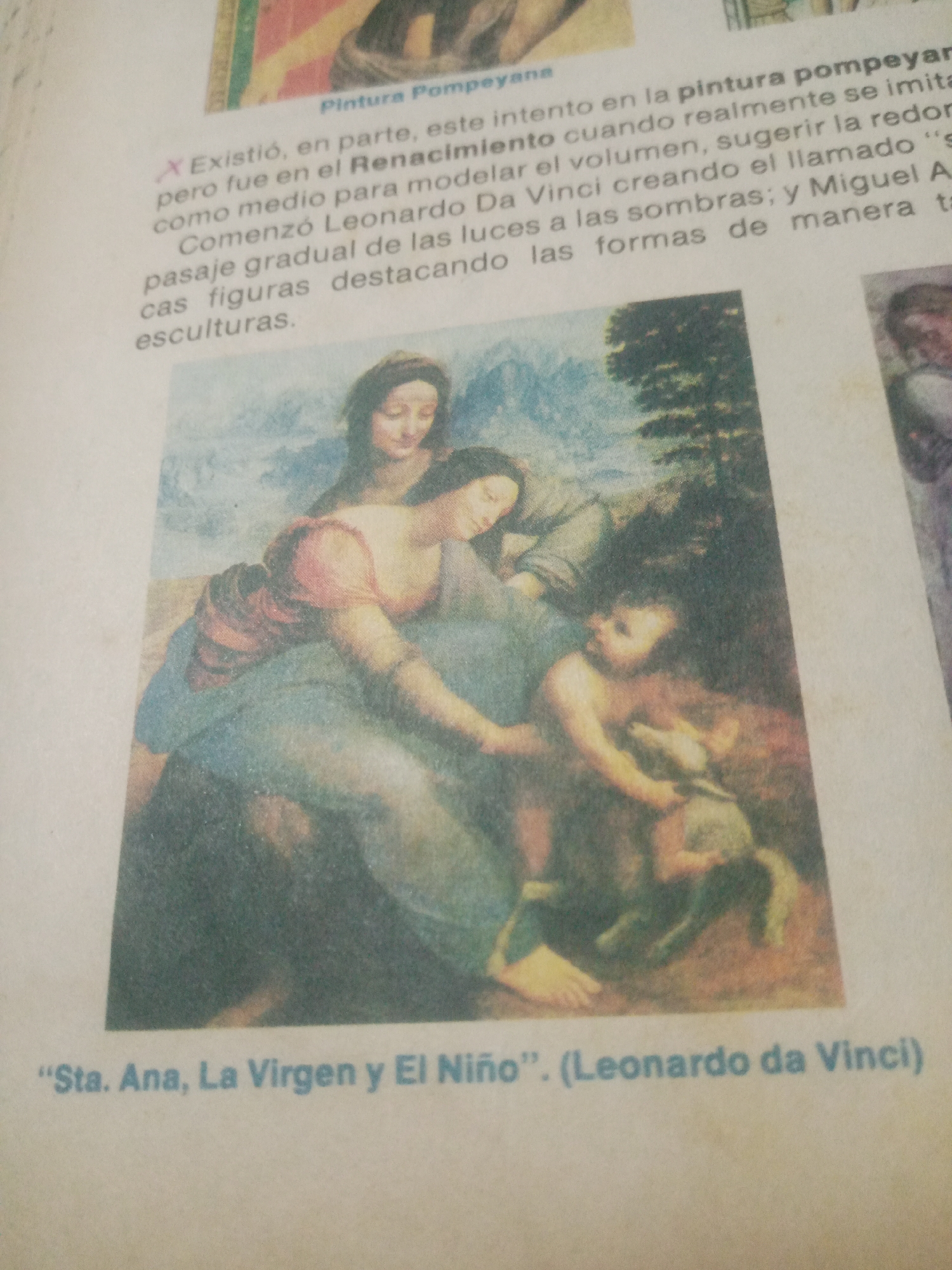 The image shows a page from a book or magazine with text and a painting. The painting depicts a religious scene with three figures: a woman, a child, and another woman. The figures are rendered in a classical style, with soft lighting and a naturalistic portrayal. The text above the painting discusses the painting's historical context and artistic techniques. Below the painting is a caption identifying it as "Santa Ana, La Virgen y El Niño" by Leonardo da Vinci. The text mentions Renaissance art and techniques like chiaroscuro. The image is a scanned reproduction, and some of the text and the painting are slightly blurry or out of focus. The painting is identified as being by Leonardo da Vinci, and the caption refers to "Santa Ana." However, there is no information in the image to suggest it is located in Santa Ana, Venezuela.