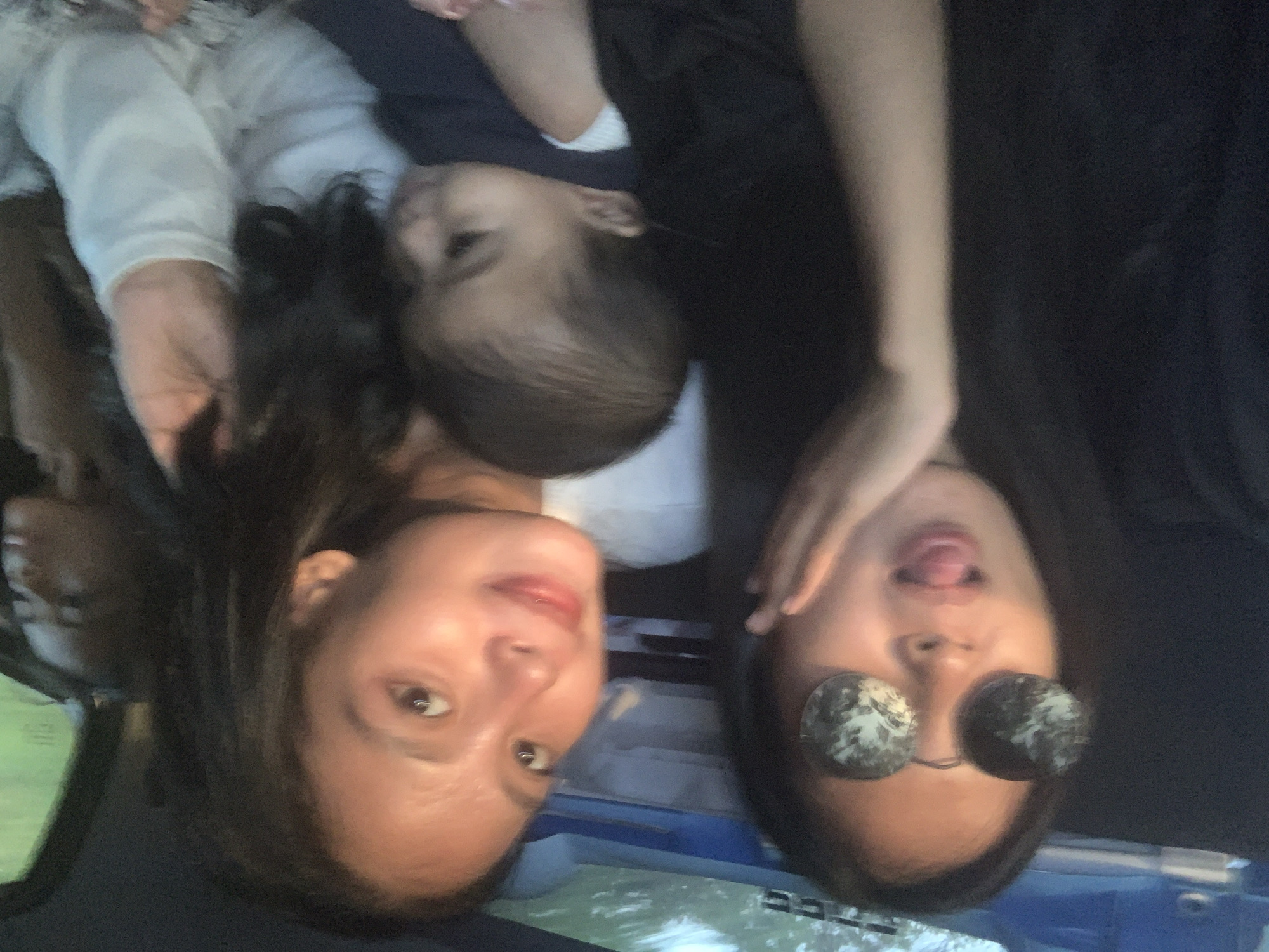 Three people are lying down together. One person, wearing round sunglasses, is sticking out their tongue. A second person is looking up with a slight smile. A child is lying between them. The location appears to be indoors, possibly a vehicle, although the exact details are limited. Batu Batu, Indonesia, is not identifiable as a specific location within the image.