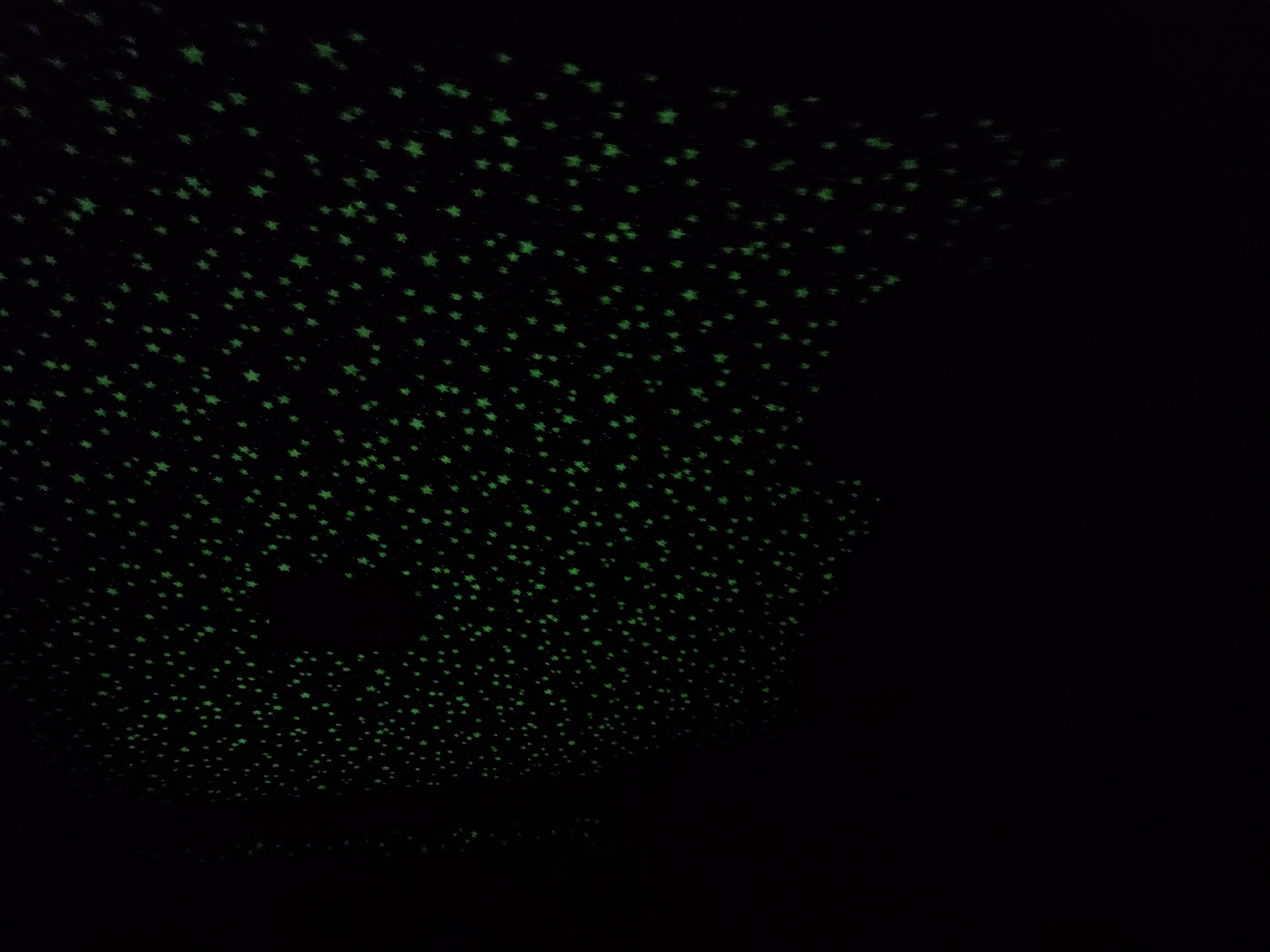 The image depicts a dark room with numerous green star-shaped lights projected onto a surface, likely a ceiling. The pattern of stars is dense, with a few dark patches where the projection is absent. The overall scene is dark, with the green stars providing the primary source of illumination. The location, Khimki, Russia, is not discernible from the visual information provided.