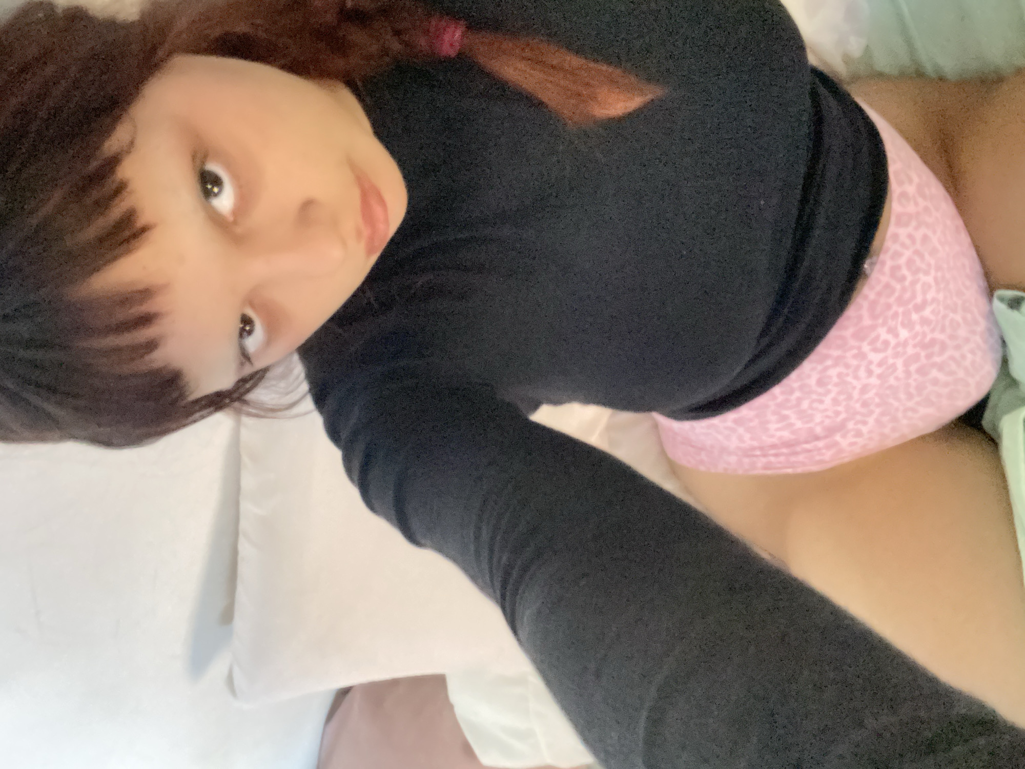 A person with dark hair and bangs, wearing a long-sleeved black shirt and pink patterned underwear, is lying on a white pillow in bed. A small portion of what appears to be a leg is visible near the bottom of the image. The location in Buenos Aires, Argentina, cannot be determined from this image.