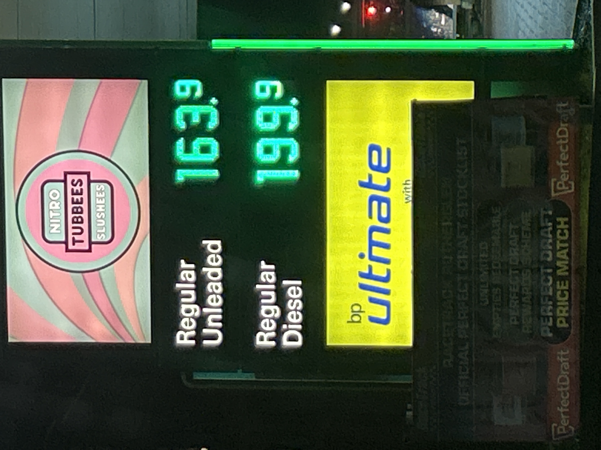 The image shows a gas station sign in Rutherglen, United Kingdom. The sign advertises "Nitro Tubbees Slushees". The price for "Regular Unleaded" gasoline is 163.9 and the price for "Regular Diesel" is 199.9. The sign also advertises "bp ultimate". Additionally, the sign promotes "PerfectDraft Price Match" and lists "Racetrack Rutherglen Official Perfect Craft Stocklist Unlimited Empties Redeemable Perfect Draft Rewards Scheme".