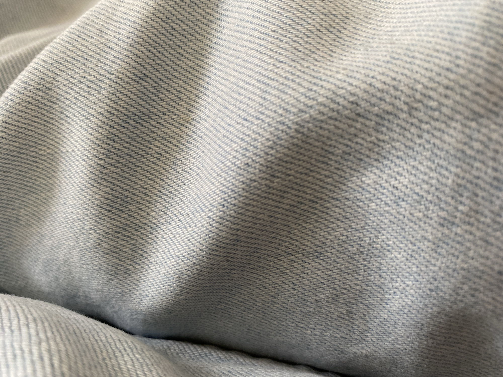 The image shows a close-up of light blue denim fabric. The fabric is folded and has a visible weave pattern. There are no indications of a specific location in Novi Sad, Serbia, or any other people, subjects, objects, actions, interactions, or environment.