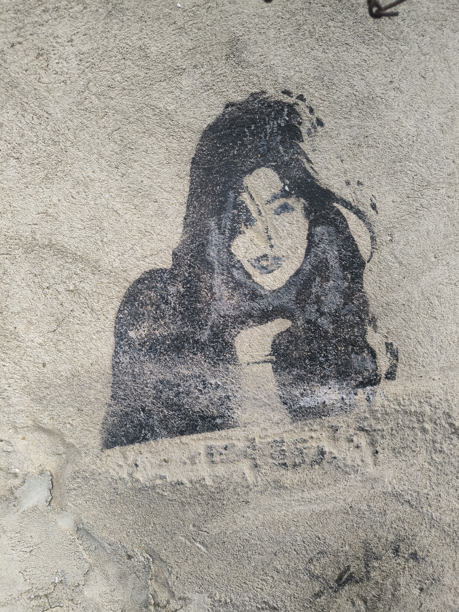 A stencil drawing of a woman is on a textured, light-colored concrete wall. The woman's head is tilted with her left hand up near her face. Her hair is long. The scene is outdoors in Tbilisi, Georgia.