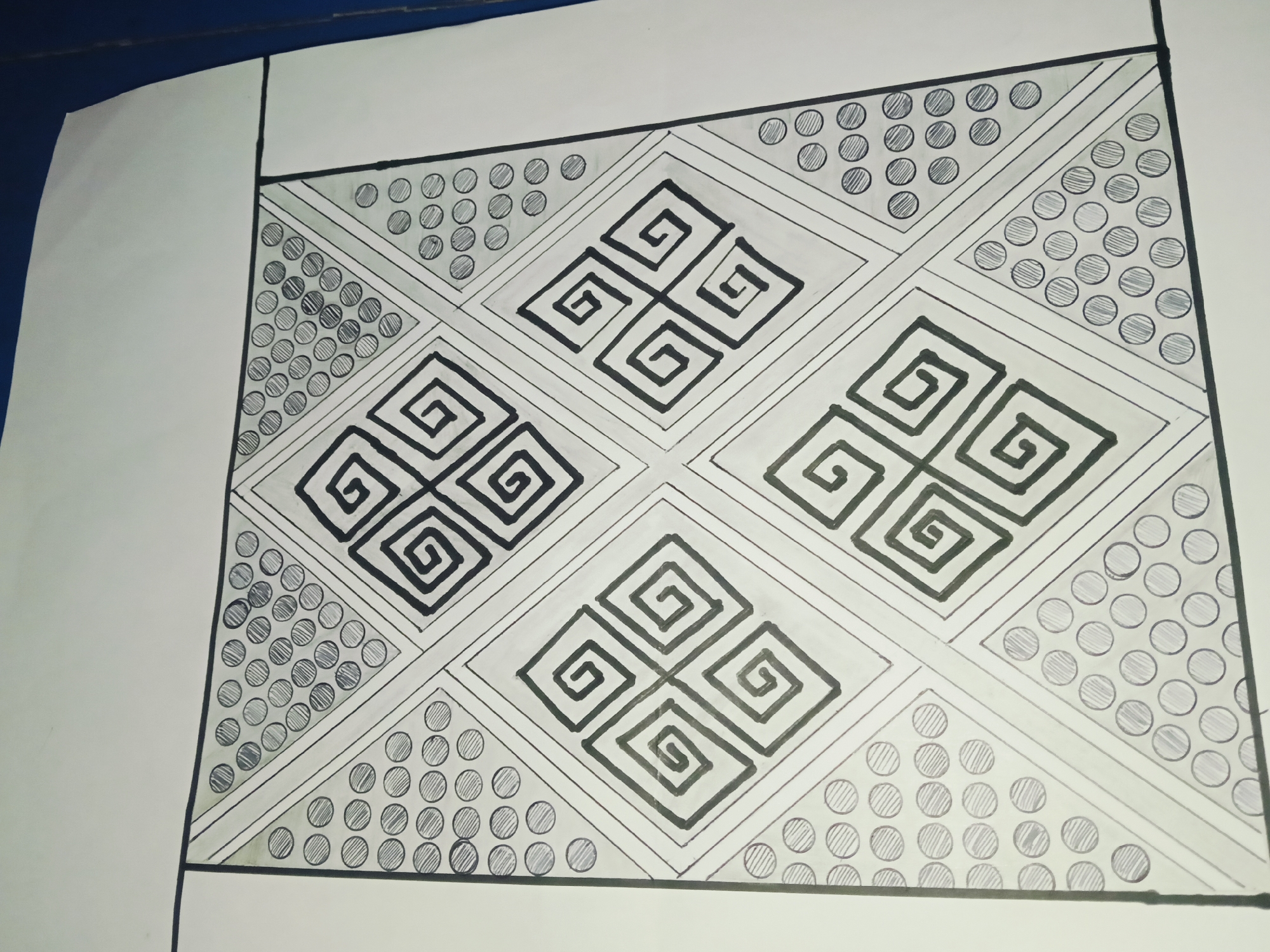 This is a black and white drawing of a geometric pattern on white paper. The pattern is enclosed within a black border. The design features a central arrangement of four diamond shapes, each containing a smaller, four-part spiral motif. These central diamonds are surrounded by triangular sections filled with rows of circles. Some circles are shaded with parallel lines, while others are left blank. The drawing appears to be done with pen or marker. The overall impression is one of symmetry and repetition. The drawing is on a white surface, and the background appears to be a dark blue surface, possibly a table or floor. There is no discernible connection to Pelanjau Jaya, Indonesia; the image depicts an abstract artwork.