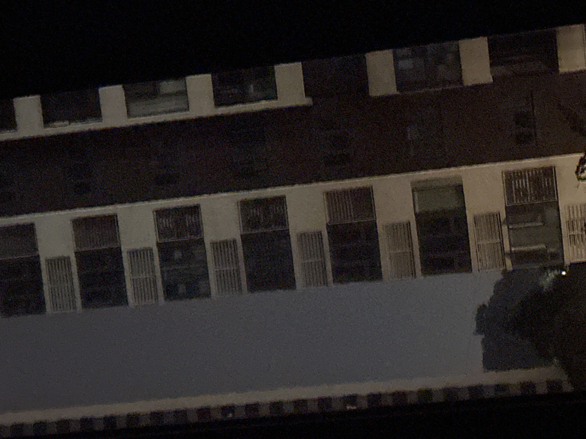 The image shows a night view of apartment buildings in the Chongqing High-tech Zone, China. The buildings are tall and modern, with many windows and balconies. The lighting is dim, with only a few lights visible from the apartments. The sky is dark and cloudy, suggesting it might be raining or foggy. The overall impression is one of a densely populated urban area at night.