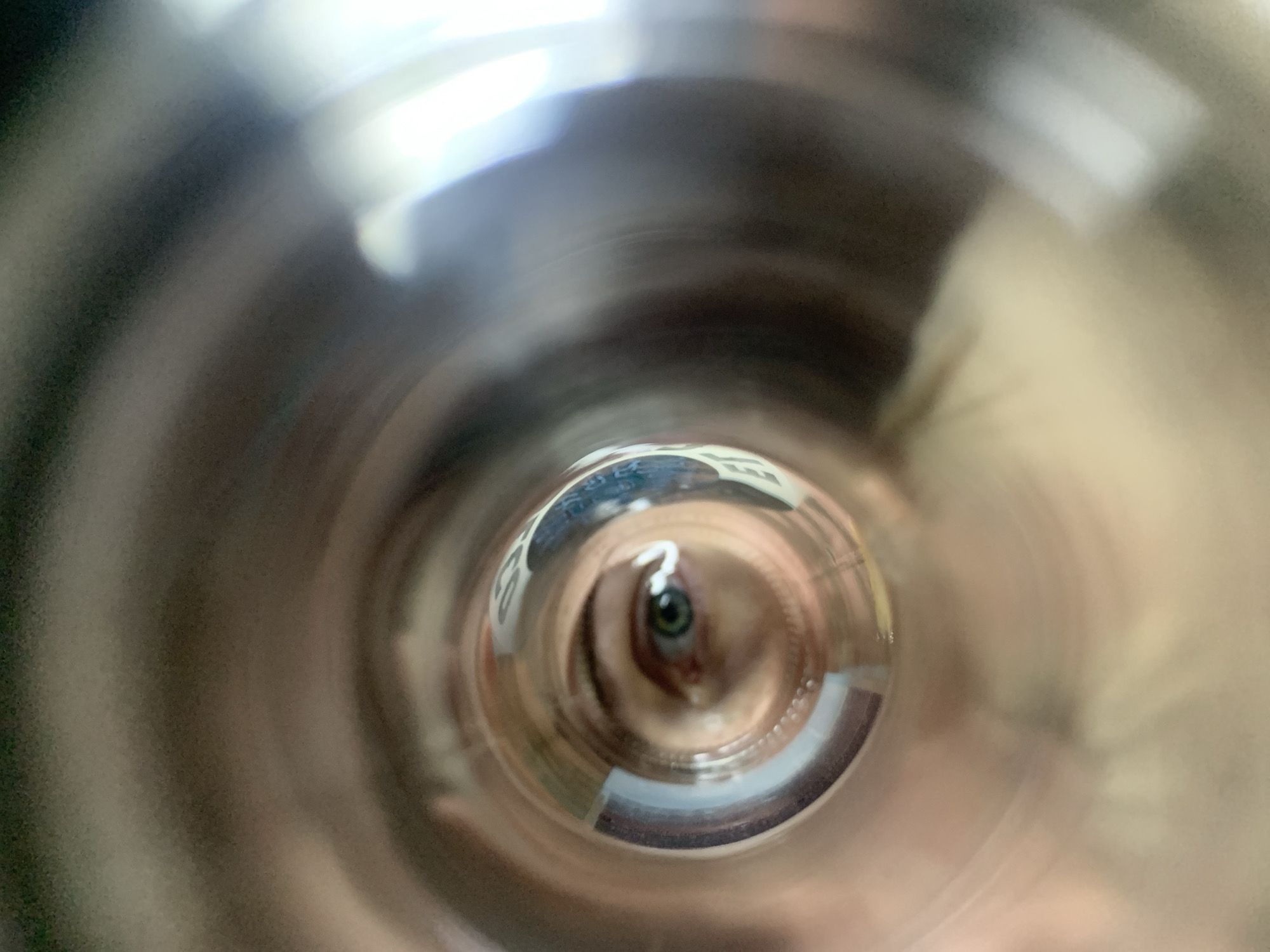 An image taken from inside a cylindrical object, likely a metal or plastic tube, looking outward. At the far end of the tube, a human eye is visible. The reflections within the tube distort the surrounding environment, making it difficult to discern specific details about the location. However, text resembling signage is partially visible, although unreadable. It is not possible to confirm the location as Chaikovsky, Russia, based solely on this image.