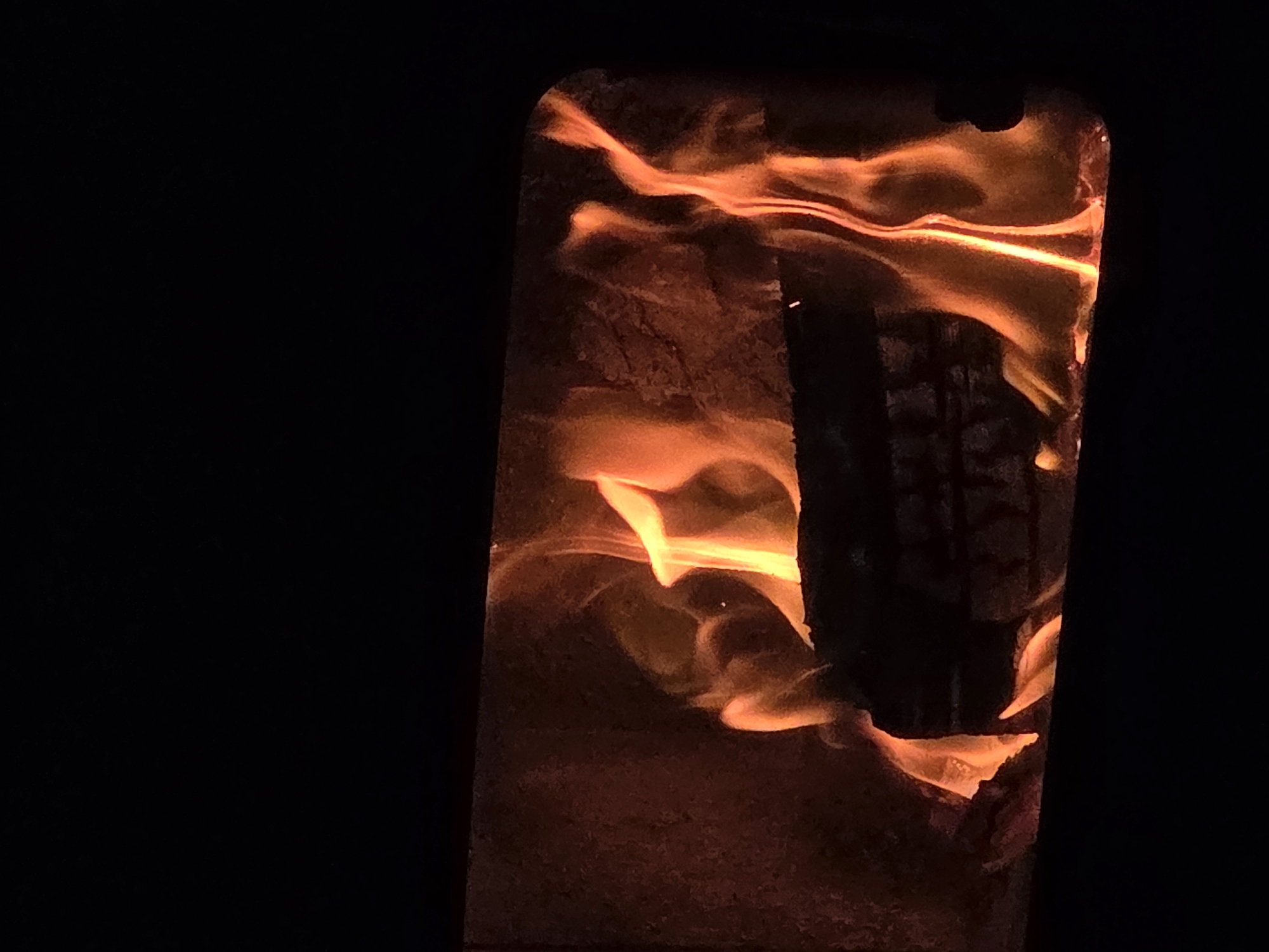 The image shows an illuminated object, possibly a decorative piece, with a flame-like pattern or design, lit from within. The object is dark brown or black with orange and yellow internal light creating the illusion of fire or embers. The background is dark, suggesting a nighttime setting or a dimly lit indoor space. There is no indication of the city of Dulovo, Bulgaria or other specific location information from the image itself. There are no people in the scene.