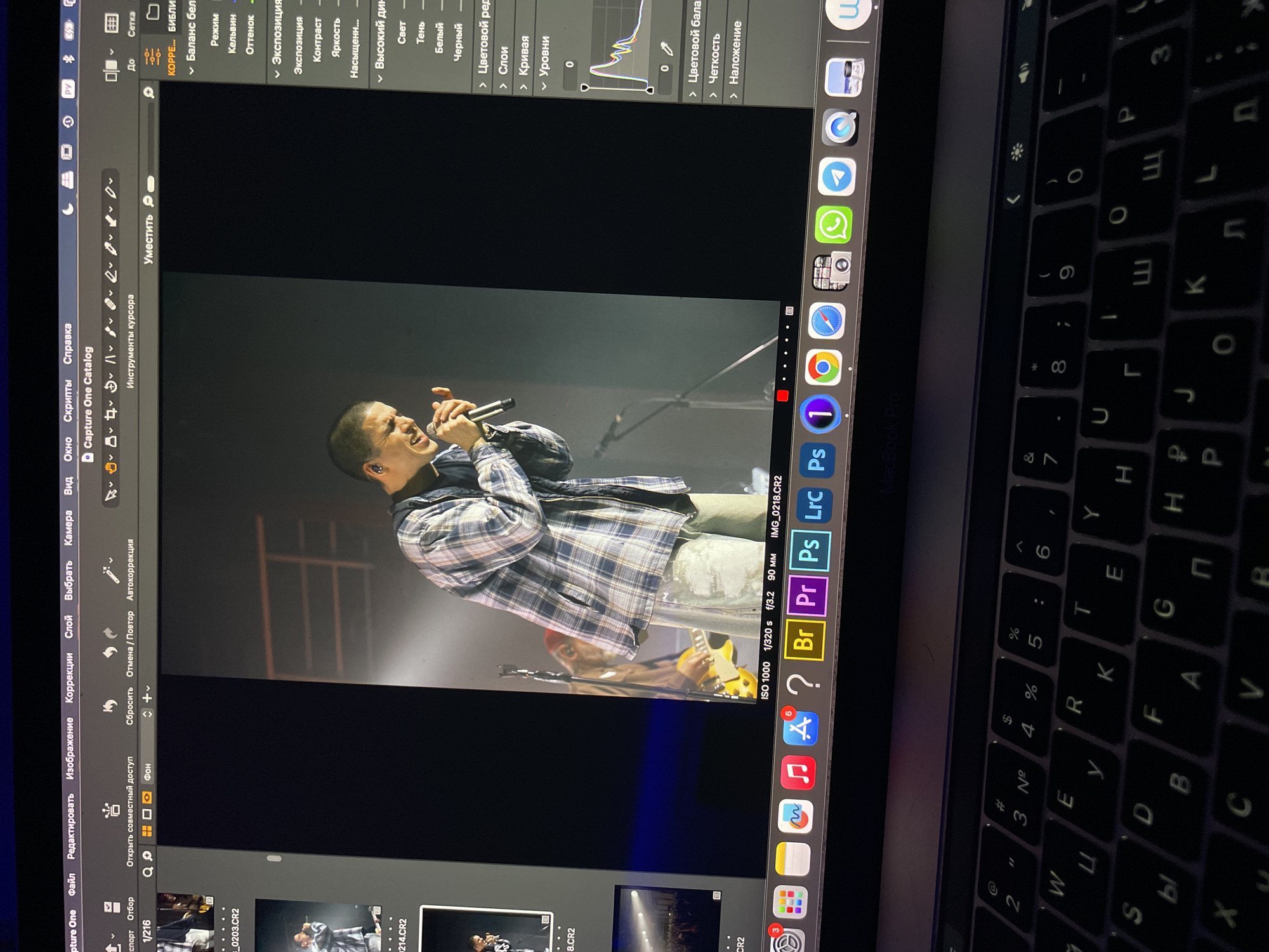 A laptop screen shows a singer holding a microphone and performing on stage. The laptop screen displays editing software (Capture One). The visible icons on the laptop's dock and the keyboard layout suggest the computer is a MacBook Pro, running in the Russian language setting. Specific parameters on the display like 'ISO 1000, 1/320s, f/3.2, 90mm' and the file name IMG_0218.CR2 indicate the picture on the editing software is being reviewed for technical aspects. Kazan, Russia is not visibly indicated in this picture.