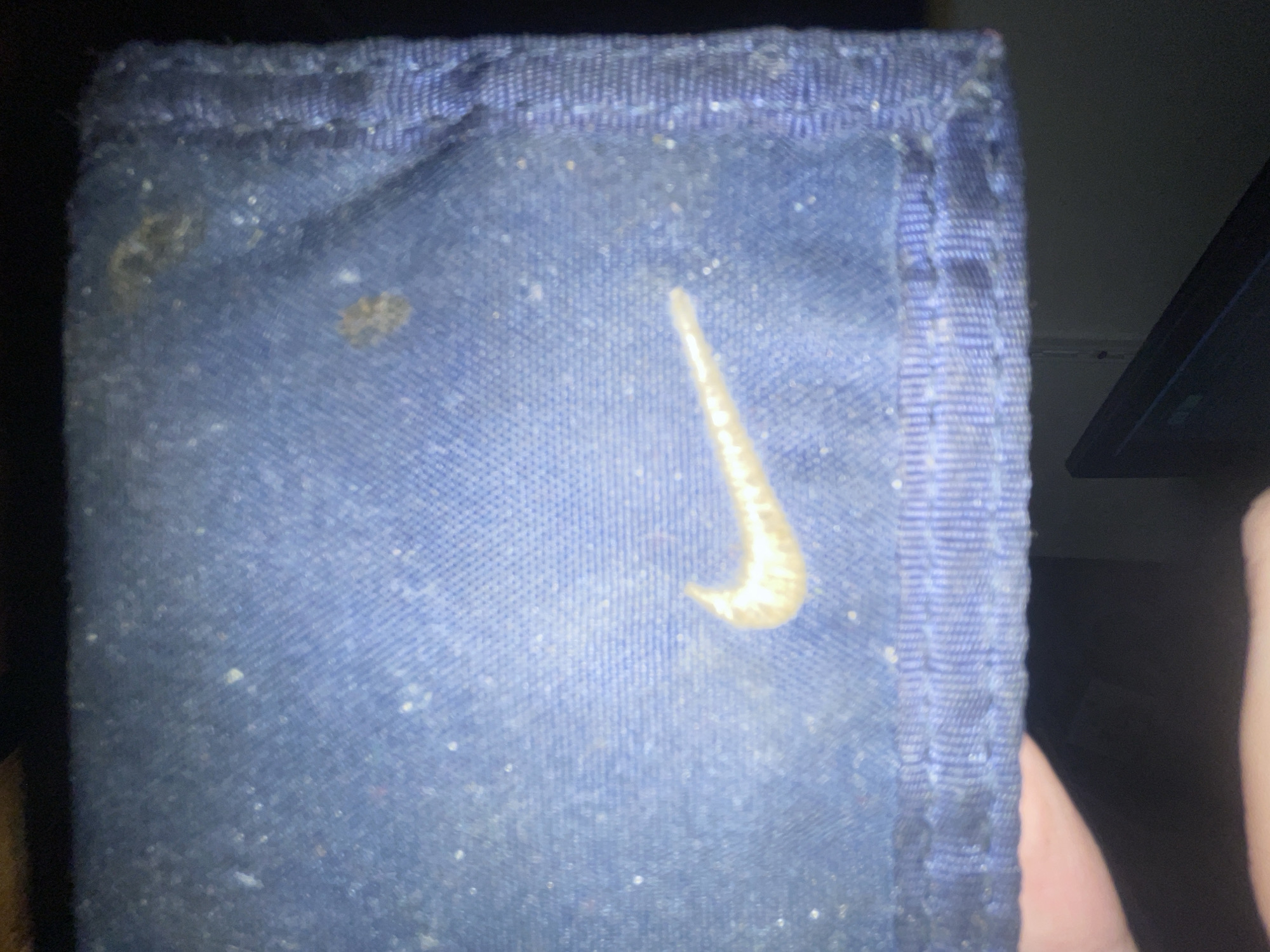 The image shows a close-up of a blue fabric wallet with a faded gold Nike logo. The wallet appears to be dusty and shows signs of wear. The background is dark, and a portion of a hand is visible in the lower left corner of the image. The context of the location in Bol'shoe Zaborod'e, Russia, is not visually represented in the image itself.