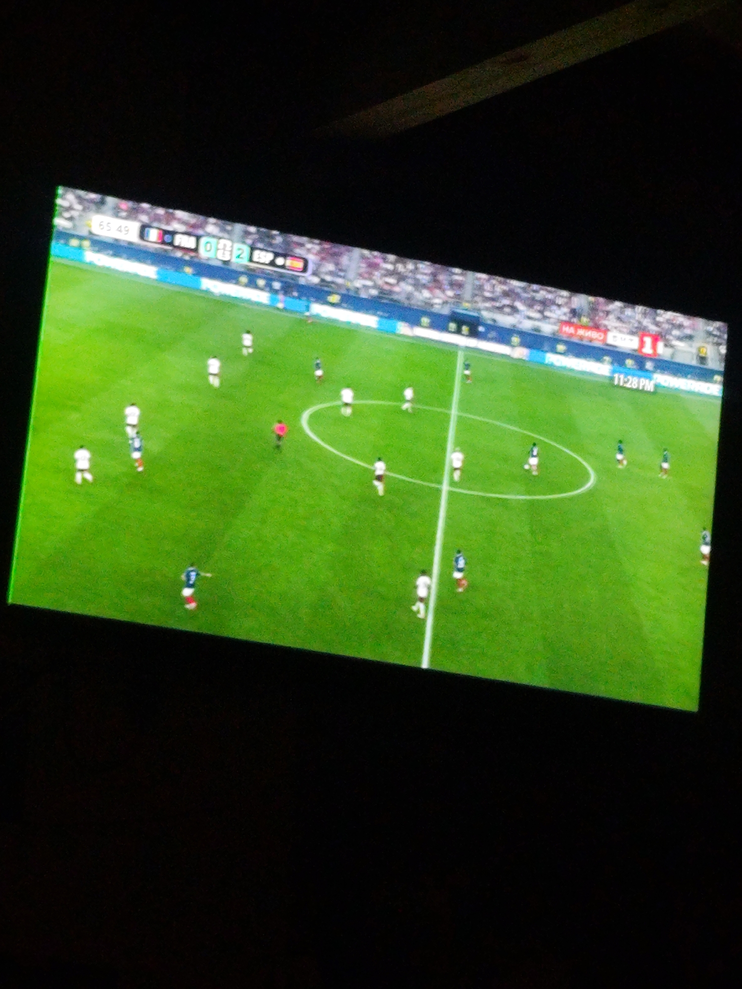 The image shows a screen displaying a soccer match. The score is visible at the top left, with "FRA" and "ESP" indicating two teams. The score shows "0-2", with the team "ESP" leading. There are players on the green field wearing white and blue uniforms. The scoreboard also shows "65:49" which might be the time of the match. The location "Prolesha, Bulgaria" is not depicted or mentioned in the image.