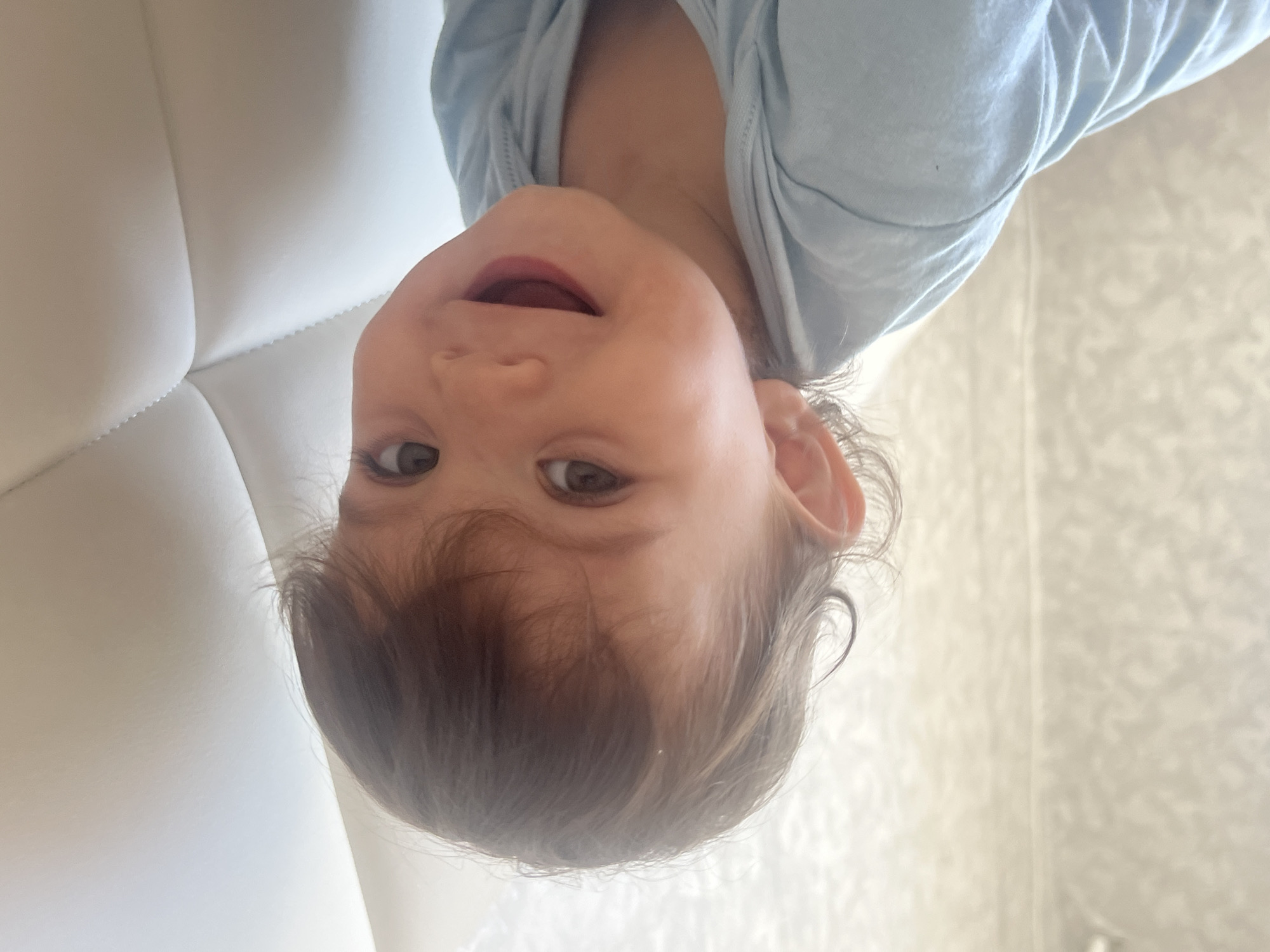 A young child with brown hair and eyes is pictured upside down, wearing a light blue garment. A white, textured surface appears to be behind the child's head. A light-colored wall with vertical patterns is also visible. The location is not discernible from the provided image. The scene does not offer any information about Elena, Bulgaria.