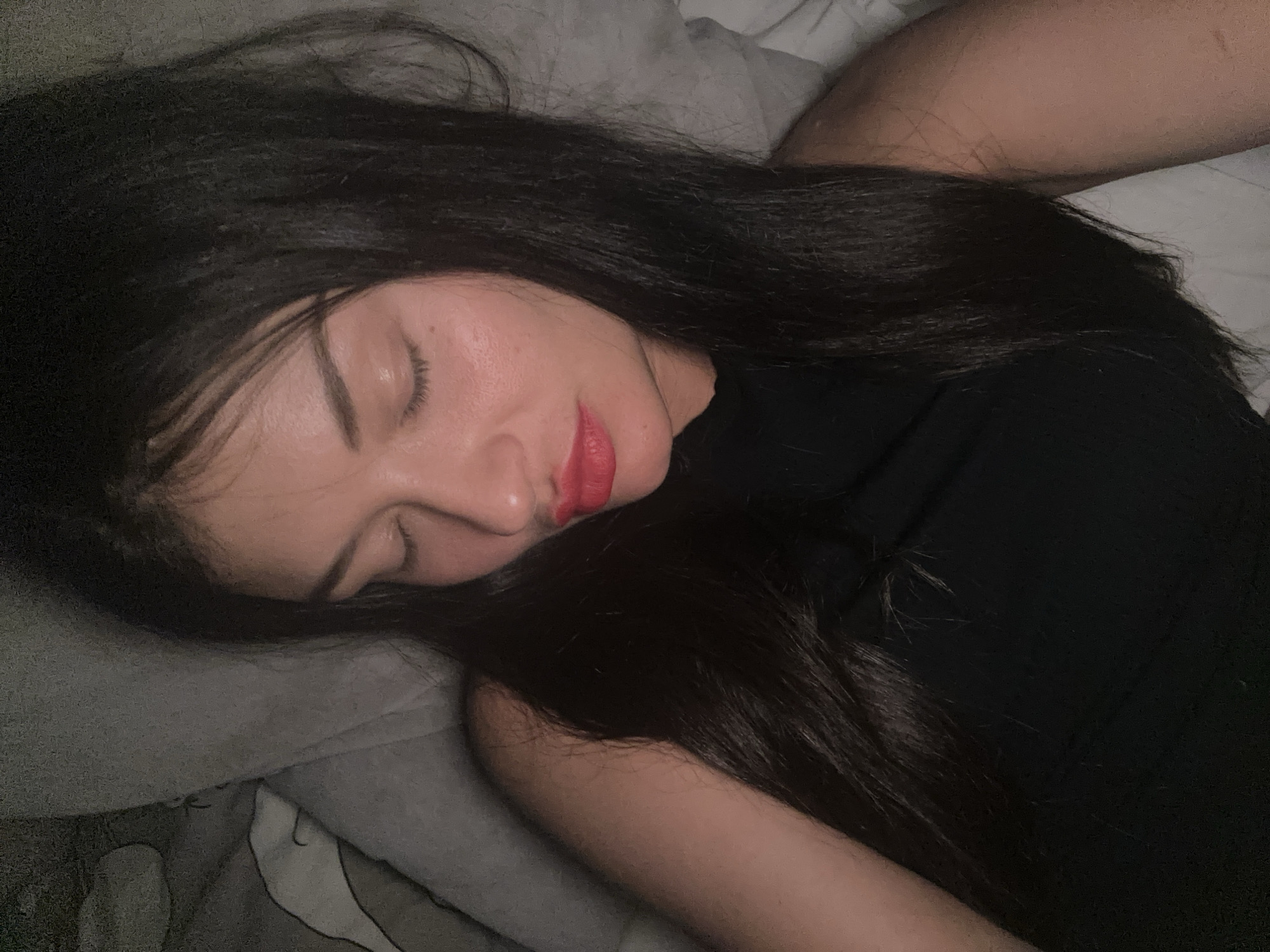 A woman with long, dark hair and red lipstick lies asleep on a pillow in a bed. She is wearing a black top. The image does not provide any information to determine if the picture was taken in Moscow, Russia.