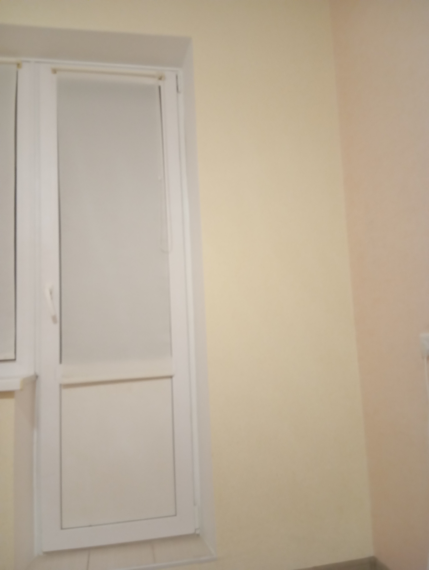 A door with a frosted glass panel is visible on the left side of the image. The door frame is white and appears to be made of PVC. The wall on the left is a pale yellow, and the wall on the right is a light pink. The floor is not visible. The scene is indoors, in what appears to be a hallway or entryway.