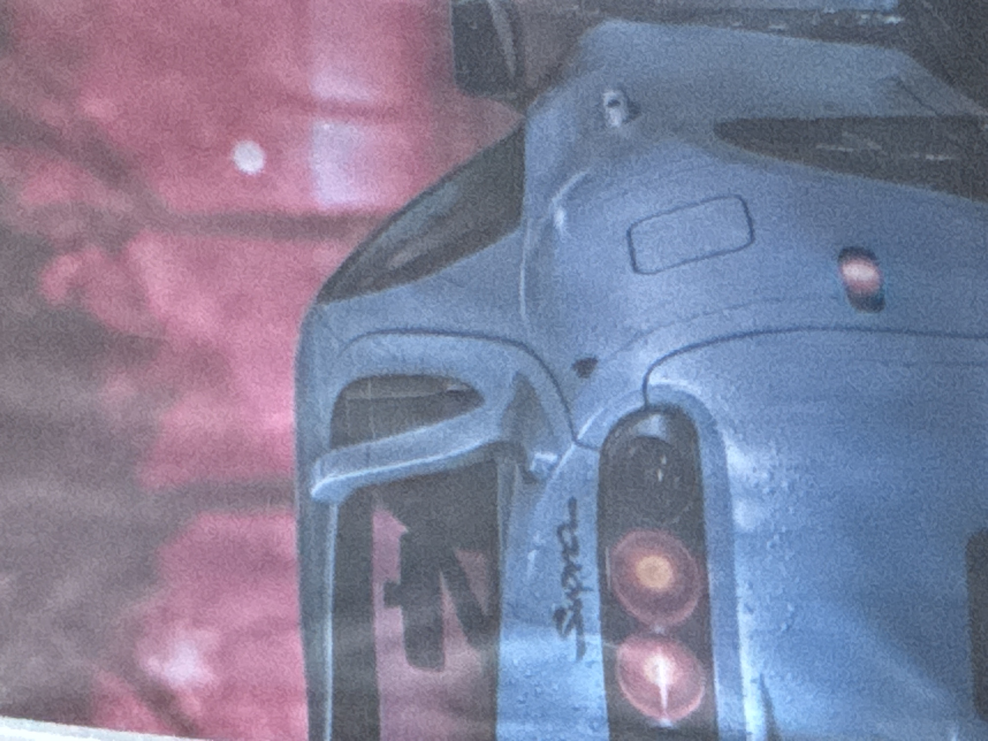 A close-up shot depicts the rear section of a blue Toyota Supra. The "Supra" logo is visible near the taillights. A portion of what looks like a building or wall is visible in the background, with a pinkish or reddish hue. The photograph seems to be taken from a medium to close distance, focusing on the car's rear. The image does not contain enough information to determine the precise location in Plovdiv, Bulgaria, or any interactions or actions within a real-world scene.