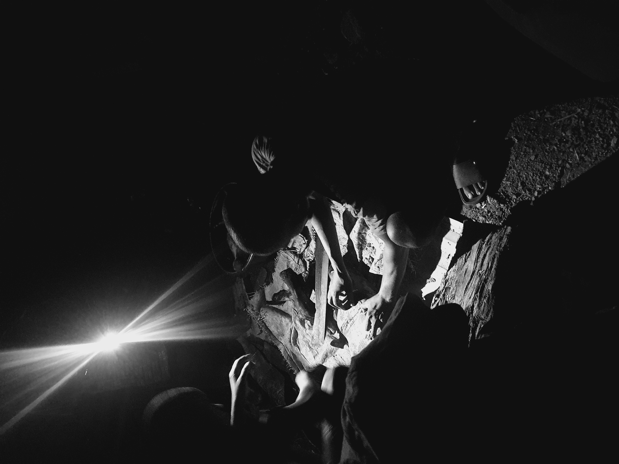 In a dimly lit or darkened environment, likely a cave or enclosed space, a group of individuals appear to be gathered around what seems to be wood or tree debris. The focal point is a pile of material illuminated by a bright light source, possibly a flashlight. The light casts strong shadows and creates high contrast in the image. There are two individuals in the image who are clearly identifiable as human beings.
The available information does not support the presence of the city of Idah, Nigeria. Further information would be needed to ascertain the location.