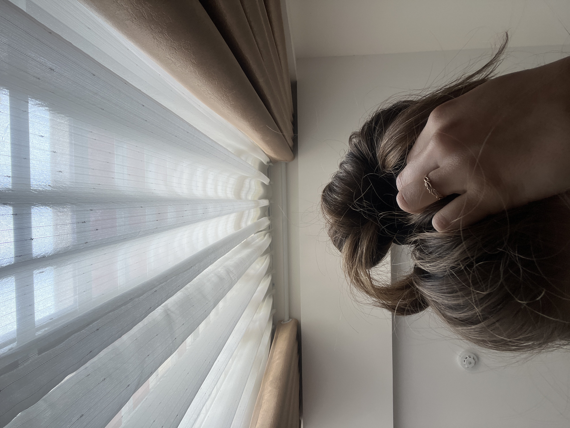 A hand wearing a ring is holding a bun of light brown hair near a window with white and brown blinds. The blinds are partially open. Part of a white wall is visible. A small, round object is on the wall near the hair.
The image does not provide sufficient information to determine the location or to confirm it is in the Nam Natural Heritage Area Trang, Vietnam.