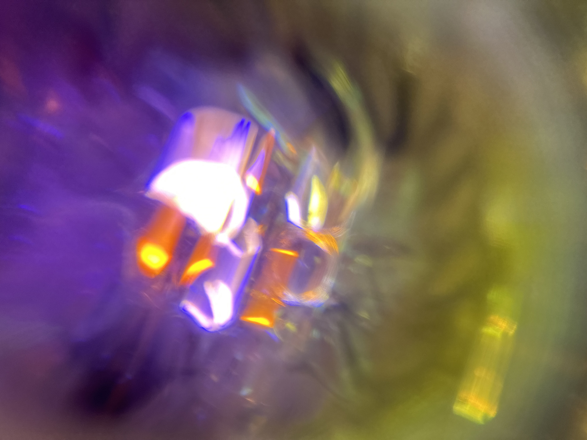 The image presents a blurred, abstract composition with a color palette dominated by shades of purple, yellow, and orange. There are no discernible people, subjects, or actions taking place. The environment is unrecognizable, and the location, a city of Unknown, Unknown, cannot be verified or identified. The image appears to be a result of either intentional artistic blurring or an error during image capture.
