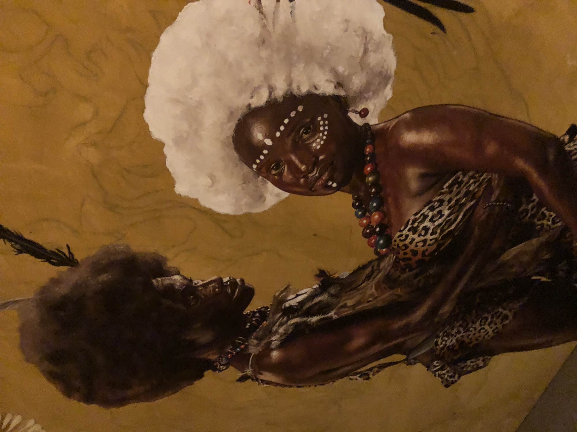 The image shows a painting featuring two dark-skinned figures against a yellowish-brown background. The figure on the top right of the painting has a large white afro, a pattern of white dots on their face, and wears a colorful beaded necklace. This figure is draped in what appears to be a leopard print garment. The second figure, positioned lower and to the left, has a dark afro with a feather sticking out. The second figure is also wearing a beaded necklace and a garment with fur or animal skin textures. The painting style appears realistic. It is not possible to determine if the image is from the city of Ado, Nigeria with the information given.
