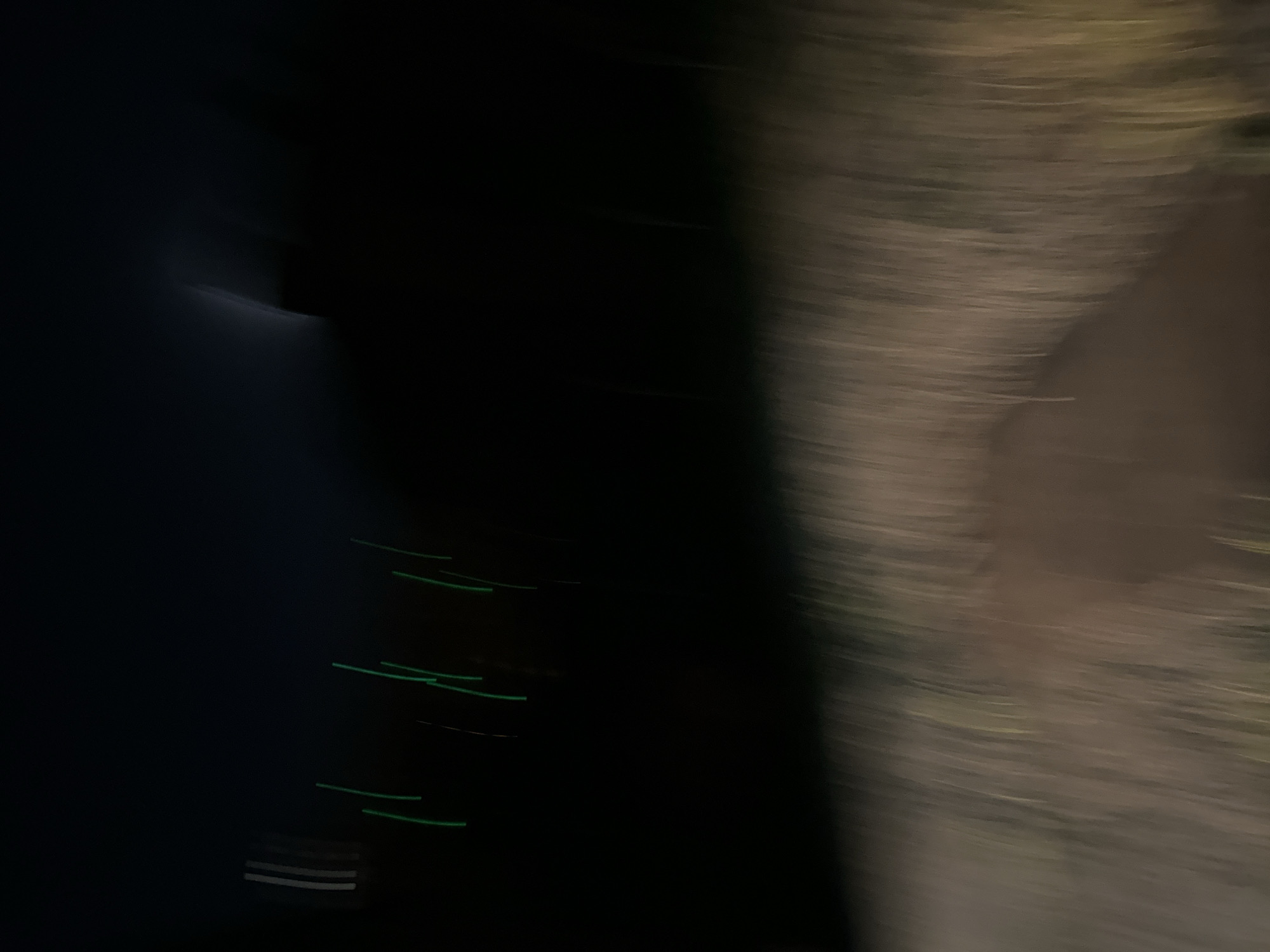 The image shows a blurred scene. The right side of the image has streaks of light brown and gray. The left side is predominantly dark, with streaks of green light. The bottom left shows a couple of stripes in light gray. It's difficult to determine the precise location in Sofia, Bulgaria, due to the blurriness. However, the streaks of light could be from headlights and taillights, suggesting a road or street.