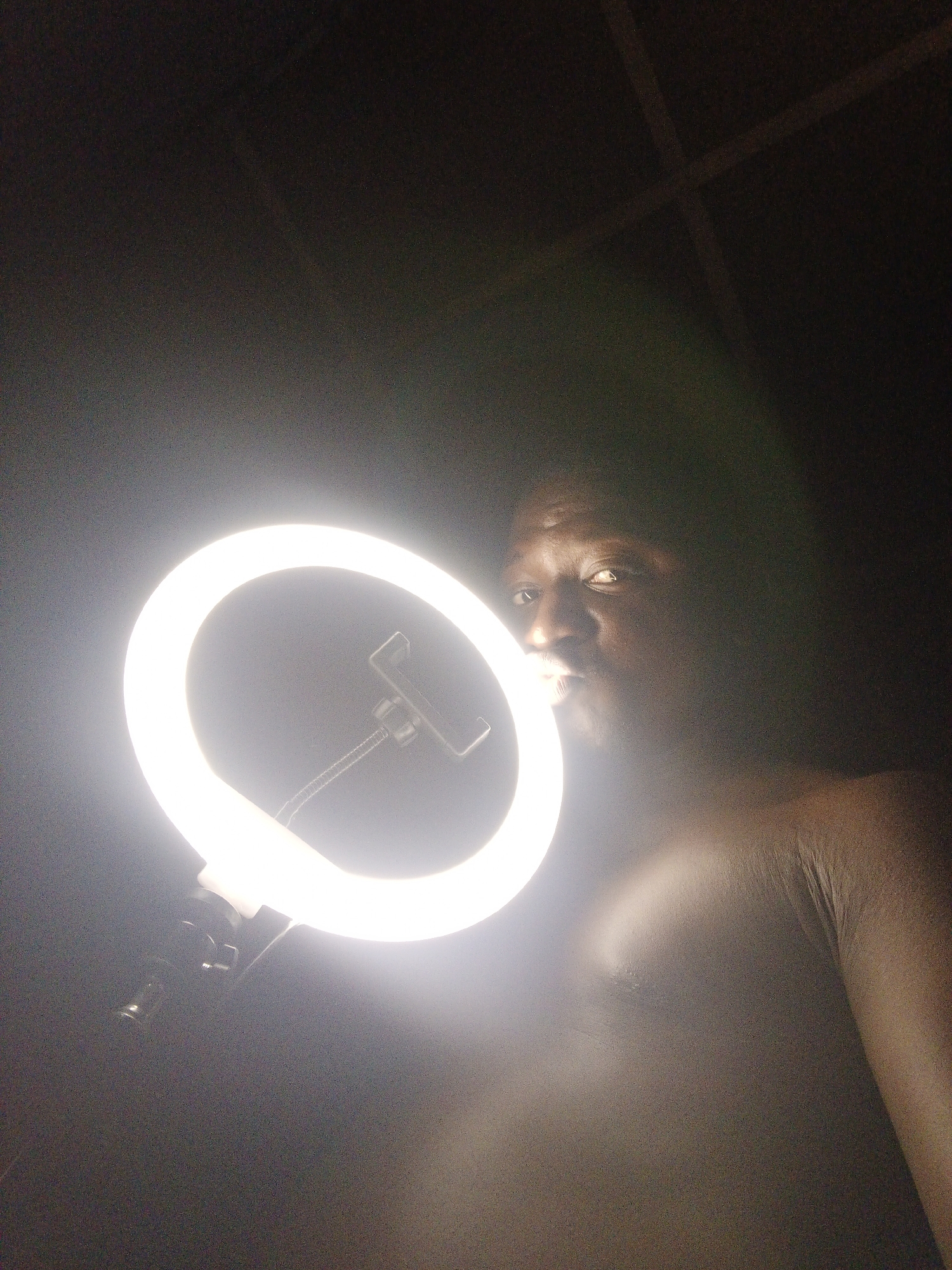 A shirtless man is holding a ring light. The location is Unknown, Unknown.