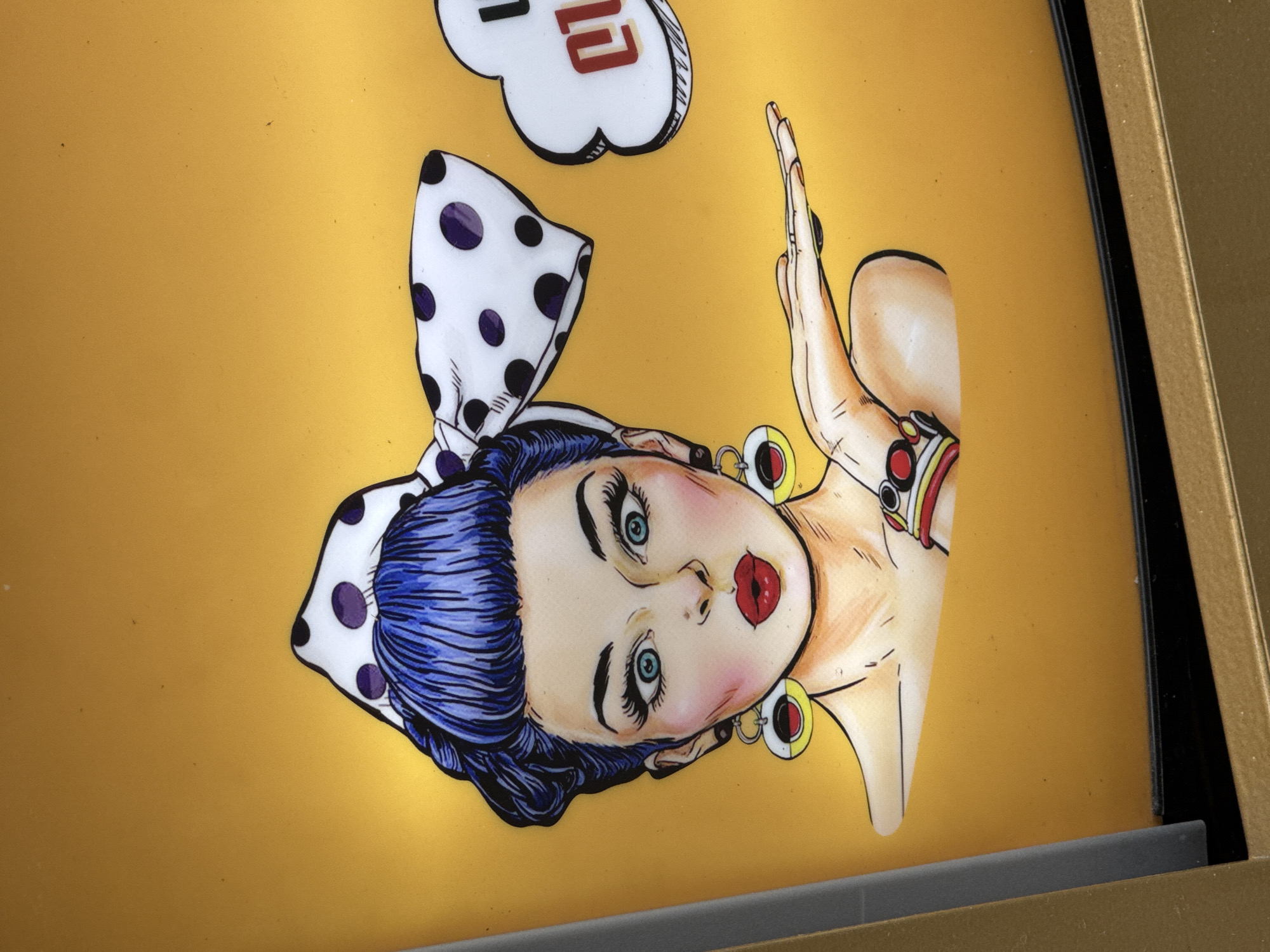 The image depicts a framed illustration of a retro-style woman with blue hair, wearing a white and purple polka-dotted headscarf. She has fair skin, red lips, and blue eyes. A cloud-shaped object with the number "12" in red is positioned above her head. She is also wearing earrings and a bracelet. The background is a solid gold color. The image is captured within a gold-colored frame with a black interior edge.