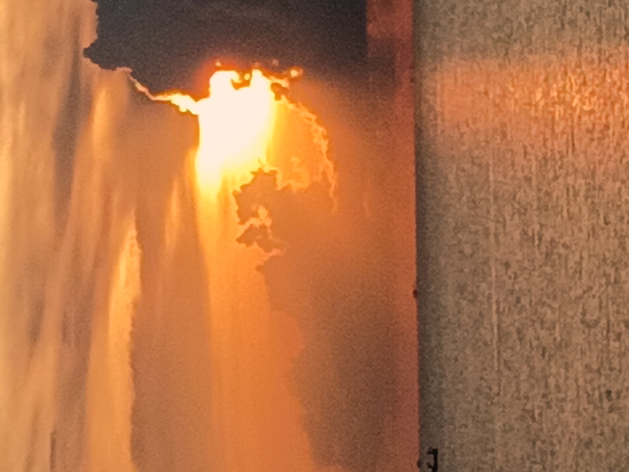 The image shows a photograph of what appears to be the sunset or sunrise peeking through clouds, casting an orange glow. The photo is close-up and seems to be of a printed image or a display, as suggested by the texture and edges visible on the right side. There are no people visible. The exact location in Baan Wok Tum, Thailand, cannot be determined based on the visual information provided.
