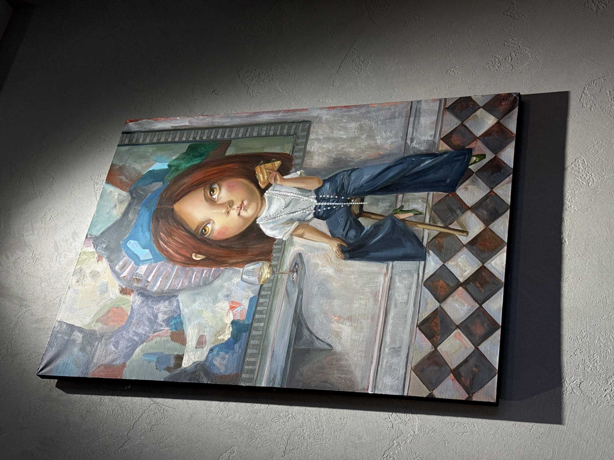 A painting of a girl eating a sandwich and sitting on a chair is hanging on a gray textured wall. The painting is tilted to the left. The girl has reddish-brown hair, tan skin, and brown eyes. She is wearing a white blouse with a pearl necklace, and blue pants. She is holding a sandwich in her left hand and sitting in a chair. A glass of wine is on the table next to her. The background of the painting is a room with a checkered floor and a window. The city of Krasnoyarsk, Russia, is not discernible from this image.