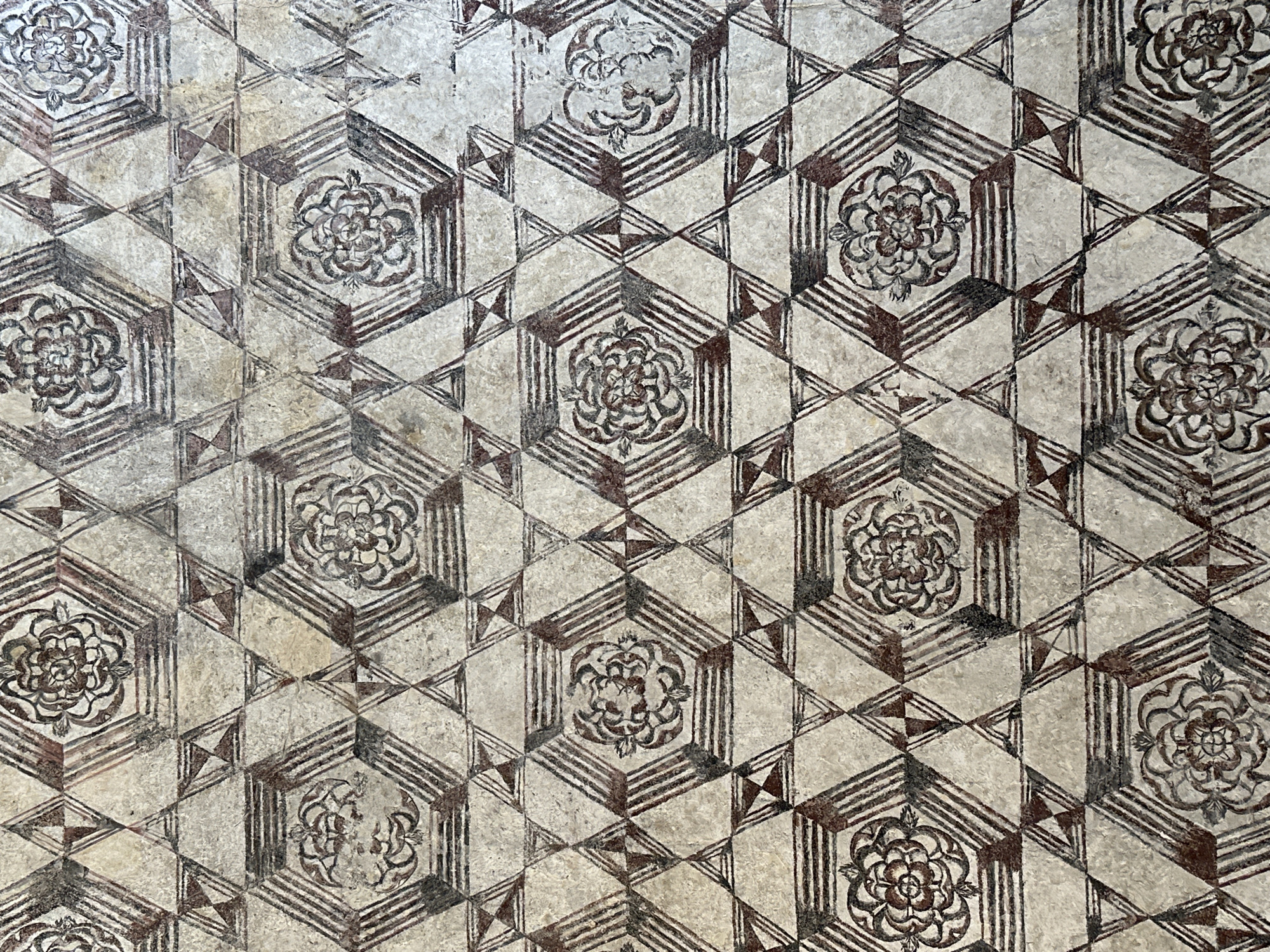 The image shows a patterned floor in Tepoztlán, Mexico. The floor is composed of repeating geometric shapes - hexagons containing floral designs and equilateral triangles. The designs are primarily in shades of brown and white, with a worn and aged appearance.