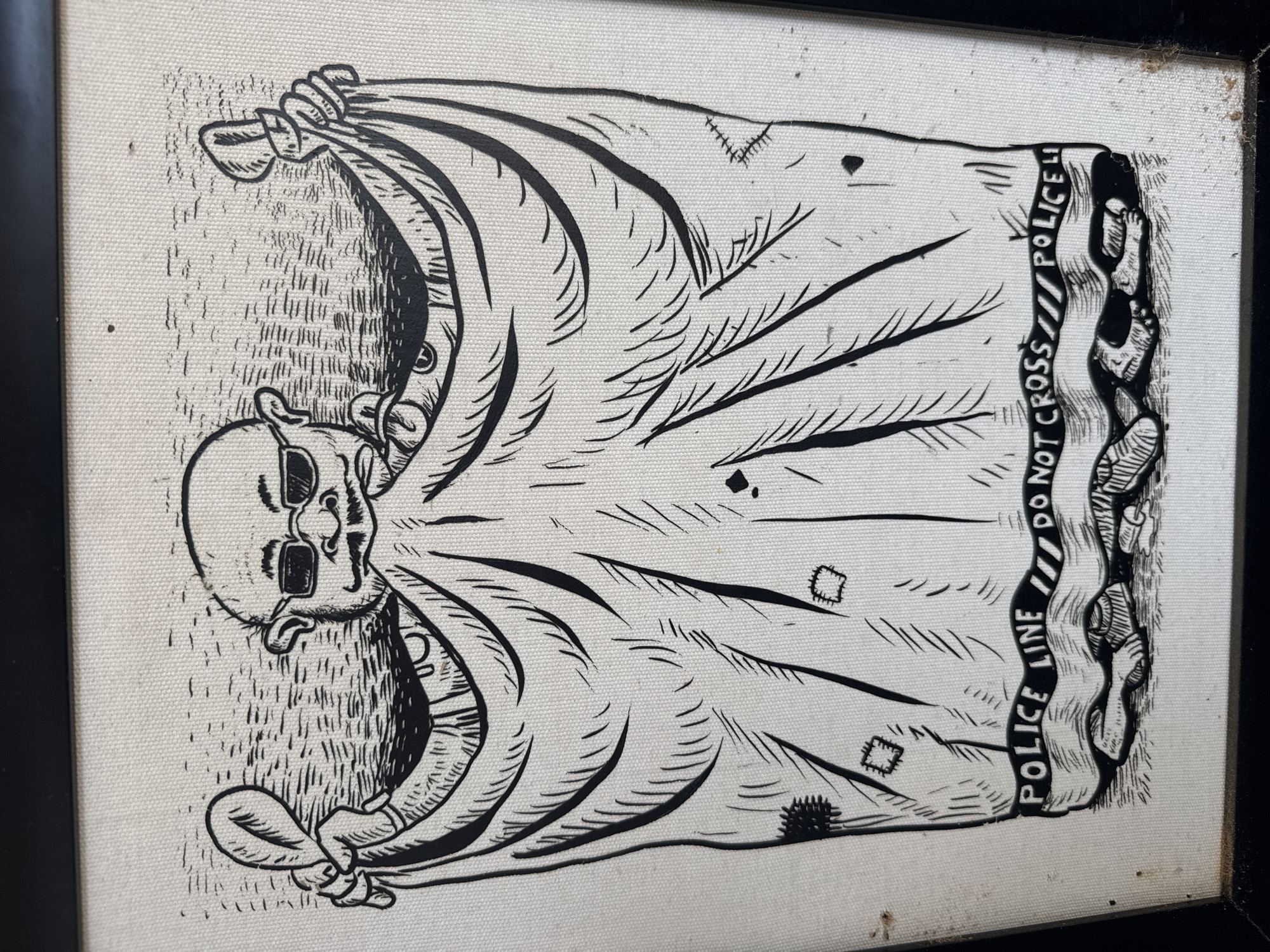 The image is a black and white illustration on a canvas background, framed in black. The illustration depicts a character, appearing to be a caricature of a person, draped in what looks like a sheet or shroud. This character is bald, wears sunglasses, and has a mustache and goatee. The shroud is held up by the character's hands, which are visible at the top corners of the image. The shroud itself is decorated with what appear to be patches, some of which are sewn on with stitch marks. At the bottom of the shroud, a black ribbon is depicted with the words "POLICE LINE DO NOT CROSS" printed on it. Below this ribbon, a pair of feet and legs, rendered in a skeletal or decomposed manner, are visible, suggesting the shroud is covering a body or is meant to represent death. The background of the illustration is a textured wash of black and white lines, possibly representing water or a hazy environment. The canvas itself appears somewhat aged, with visible texture and some minor imperfections or stains.
This image does not contain any elements that would allow for its location to be identified as Banda Aceh, Indonesia. The scene is entirely an artistic representation and does not depict any recognizable landmarks, cultural elements, or geographical features specific to any particular city.