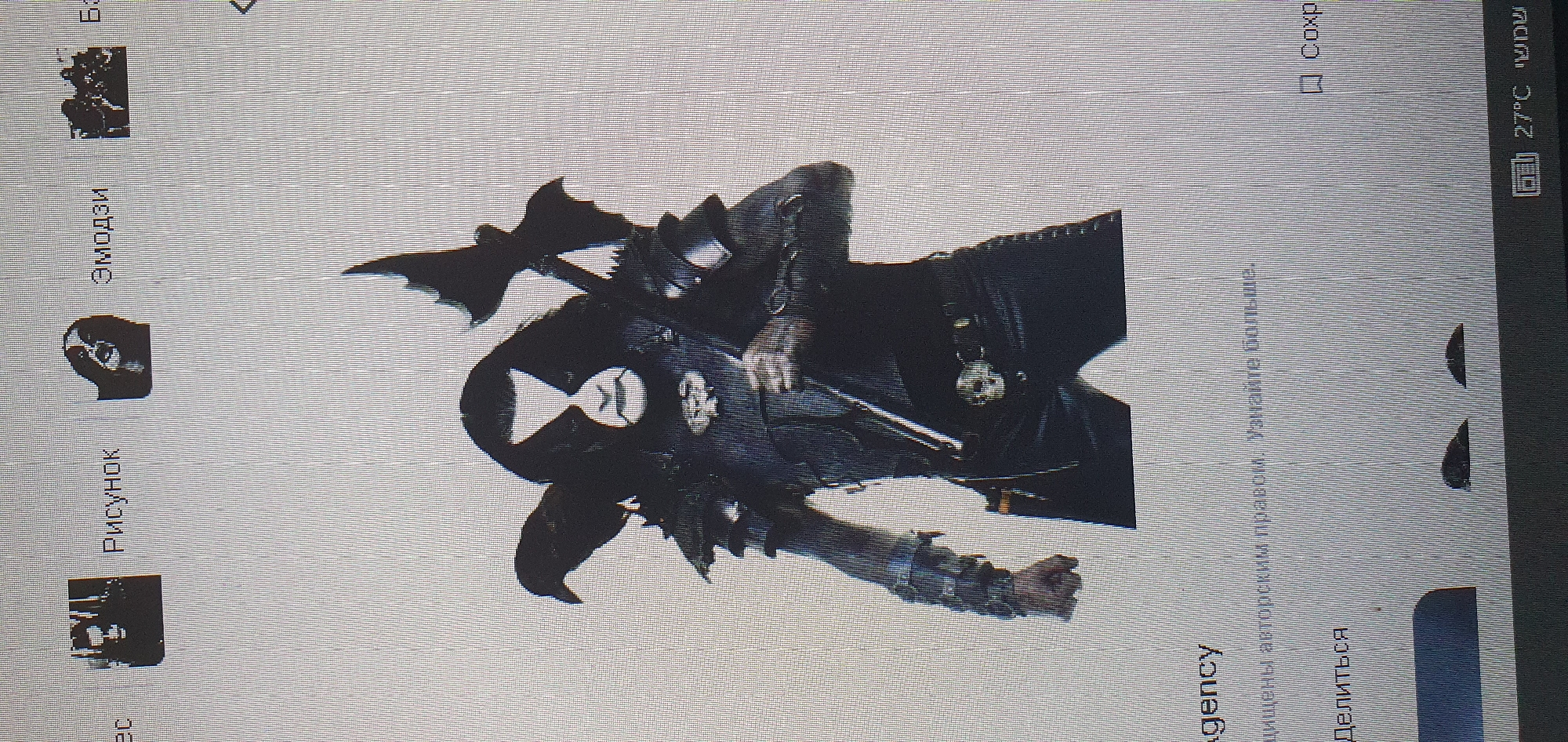 The image shows a close-up of a computer screen displaying a black and white graphic of a person in dark, elaborate attire with face paint. The person has long black hair and is adorned with spiked shoulder pads and a belt buckle with a skull design. A crow is perched on the person's left shoulder, and a weapon with bat-like wings is held over the person's right shoulder. At the bottom of the screen, text is visible in Russian, and in the bottom right corner, a temperature reading of "27°C" is displayed next to Hebrew text. The overall image appears to be a screenshot taken from a computer interface, not a photograph of a physical location in Bat Yam, Israel.