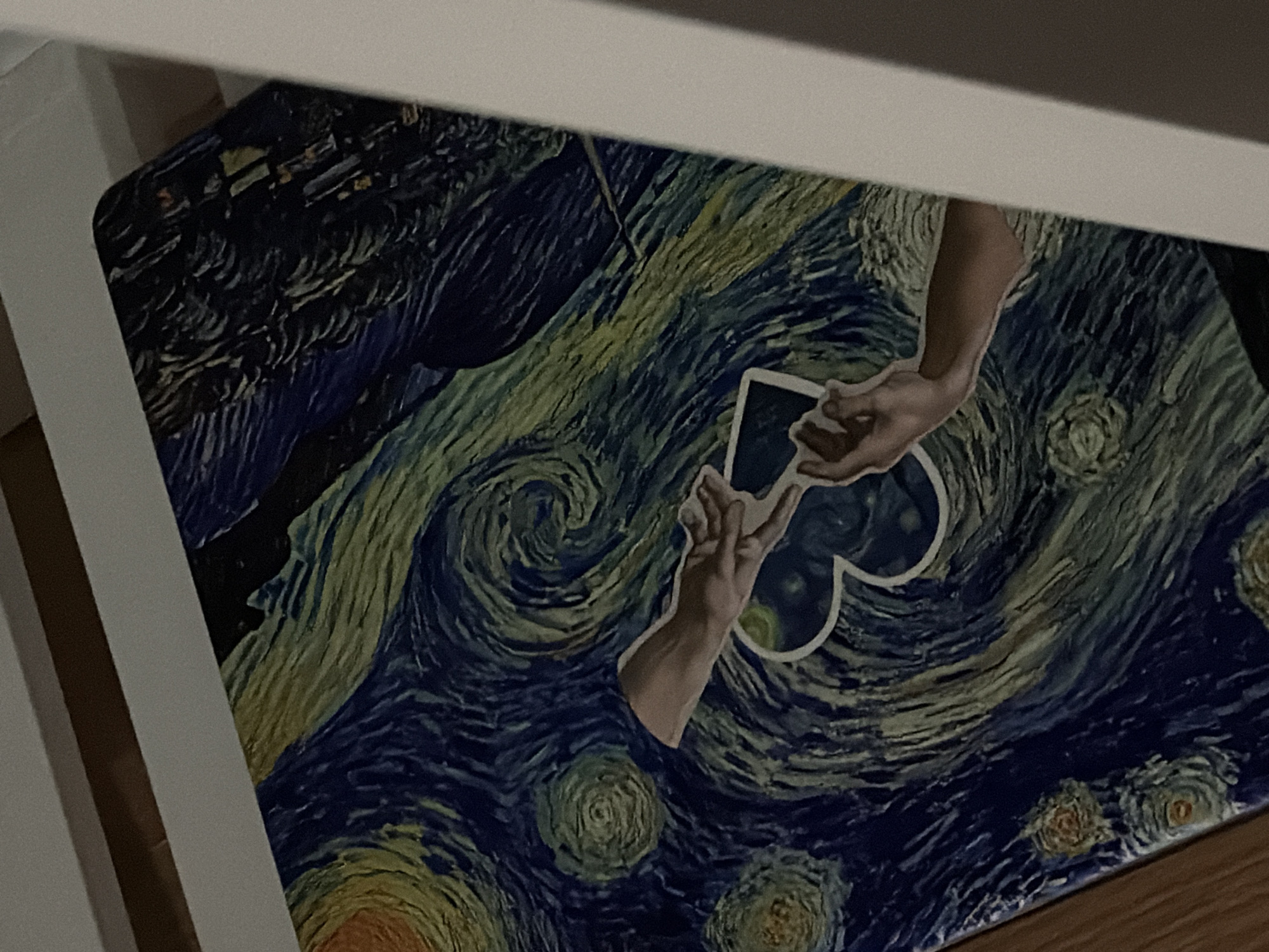 A close-up shows a portion of a Starry Night-themed object, possibly a notebook or a decorative box, with two hands reaching out to each other in front of a heart-shaped design in the center. This item appears to be located indoors, possibly on a desk or shelf, as suggested by the presence of a white ledge in the upper and left parts of the frame. The photo was taken from an elevated angle. The precise location in Morton Grove, United States of America, cannot be determined from this image.