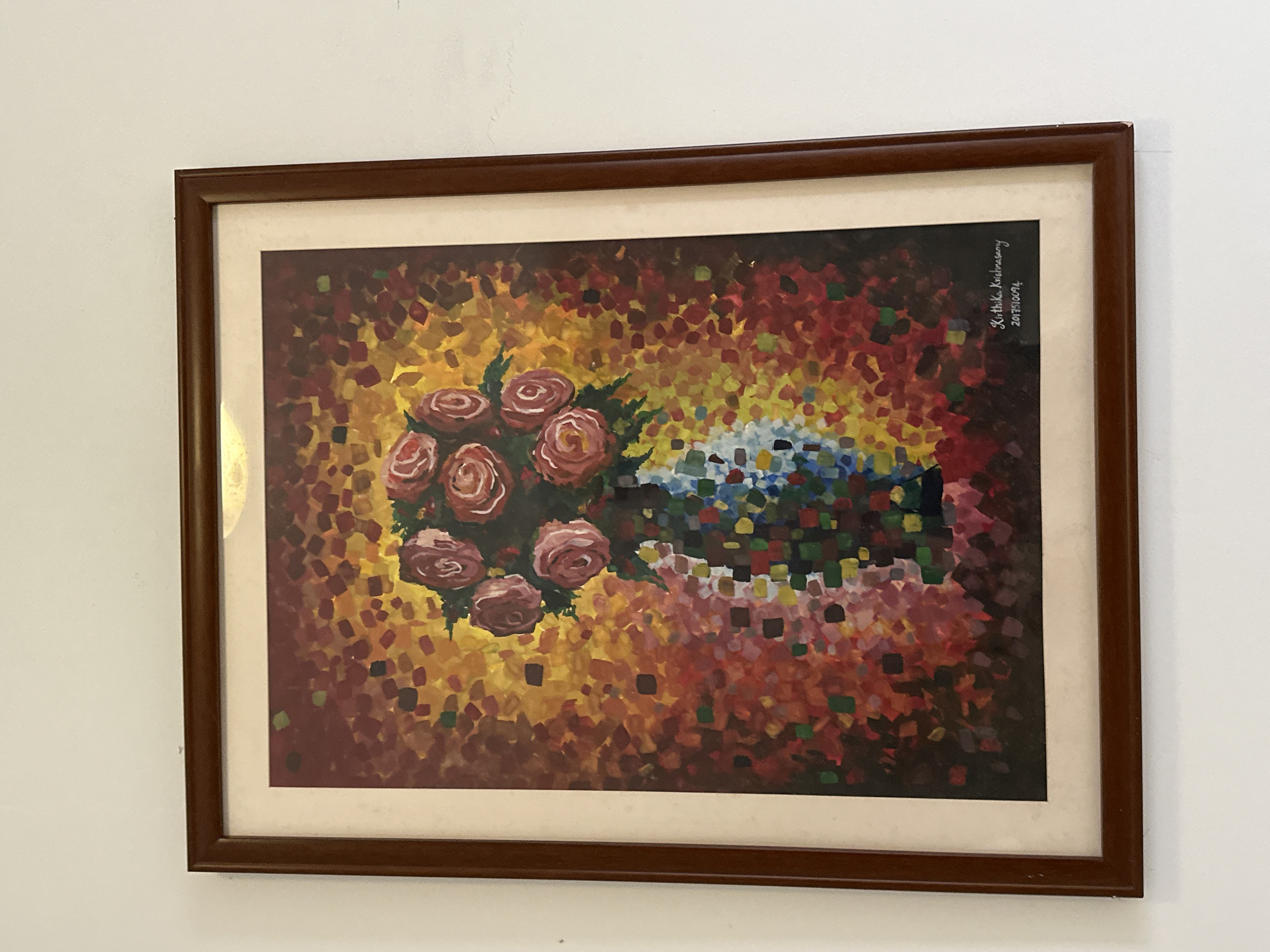 A framed painting hangs on a white wall. The painting depicts a bouquet of roses in shades of red and pink, alongside a collection of blue and white flowers. The background of the painting is a mosaic of red, orange, yellow, and brown squares. The painting is signed "Kirthika Krishnaswamy 2017/10/04" in the upper right corner. The frame is dark brown. The location is unknown, as the image does not provide information regarding the city of Chongqing High-tech Zone, China.