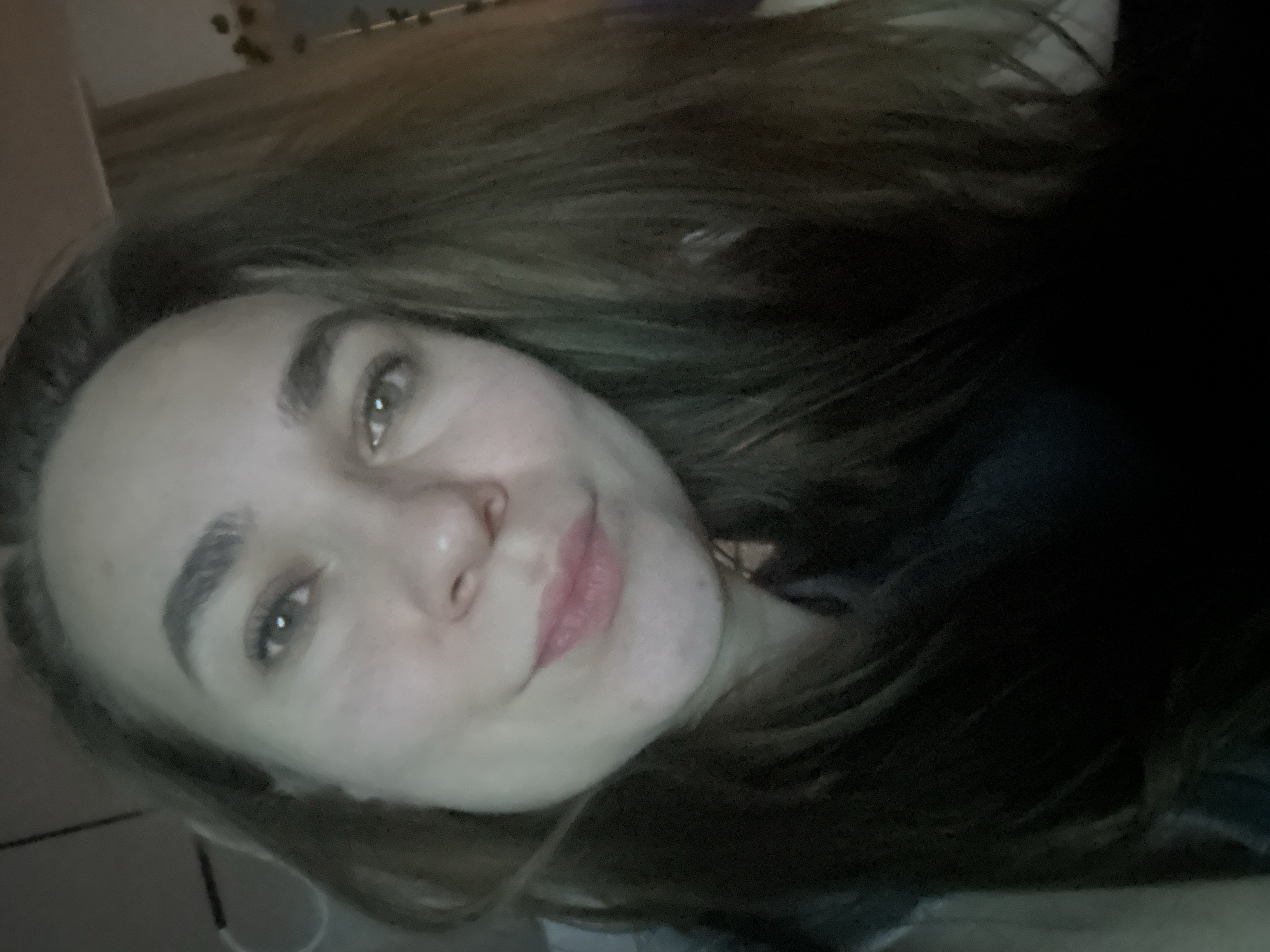 A selfie shows a fair-skinned woman with light brown hair looking at the camera. The background is dark and indistinct. There is no evidence to suggest the image was taken in Kharnavy, Russia.