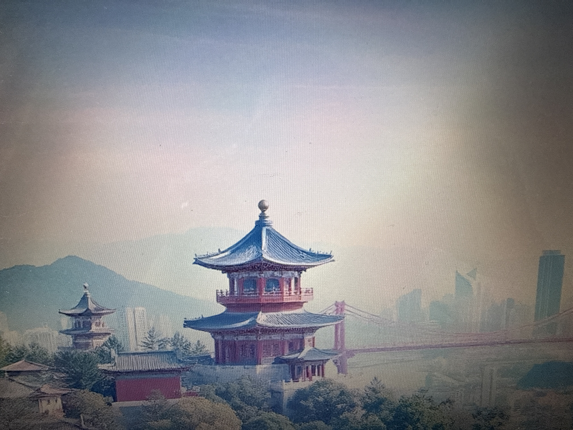 The image depicts a traditional East Asian pagoda situated on a hill overlooking a modern city skyline. The pagoda, with its multi-tiered, blue-tiled roof and red-painted levels, is the central focus. Surrounding the pagoda are lush trees and smaller traditional buildings. In the background, a suspension bridge spans across a body of water, connecting to a city characterized by skyscrapers. The atmosphere is hazy, suggesting it might be early morning or late afternoon, or due to pollution. The image does not provide any contextual information or visual cues to place it in Pushkino, Russia.