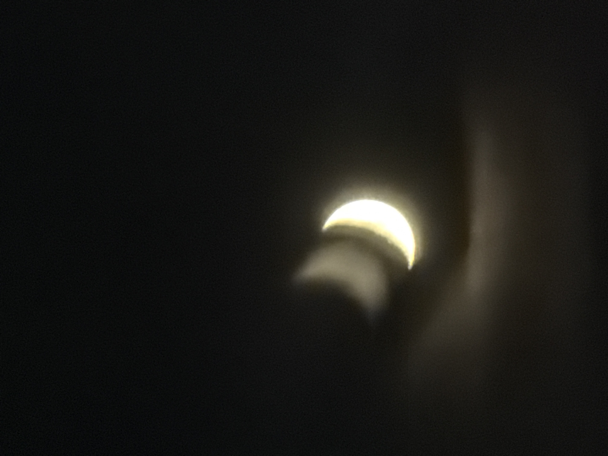 The image shows a dark, blurry night sky with two faint crescent moon shapes. The shapes are illuminated by a soft, yellow light and appear to be overlaid on a dark background. The overall impression is of a hazy or out-of-focus photograph of the moon. There is no discernible city, location, or any other identifiable features in the image.