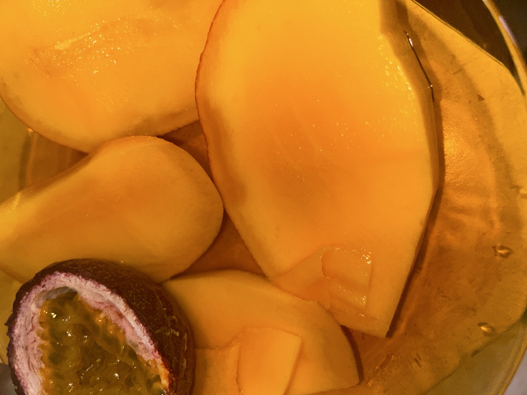 The image shows a close-up of cut mango and half a passion fruit inside a container. The mango is peeled and sliced. The passion fruit is cut in half, revealing its pulp. The scene takes place in Varna, Bulgaria.