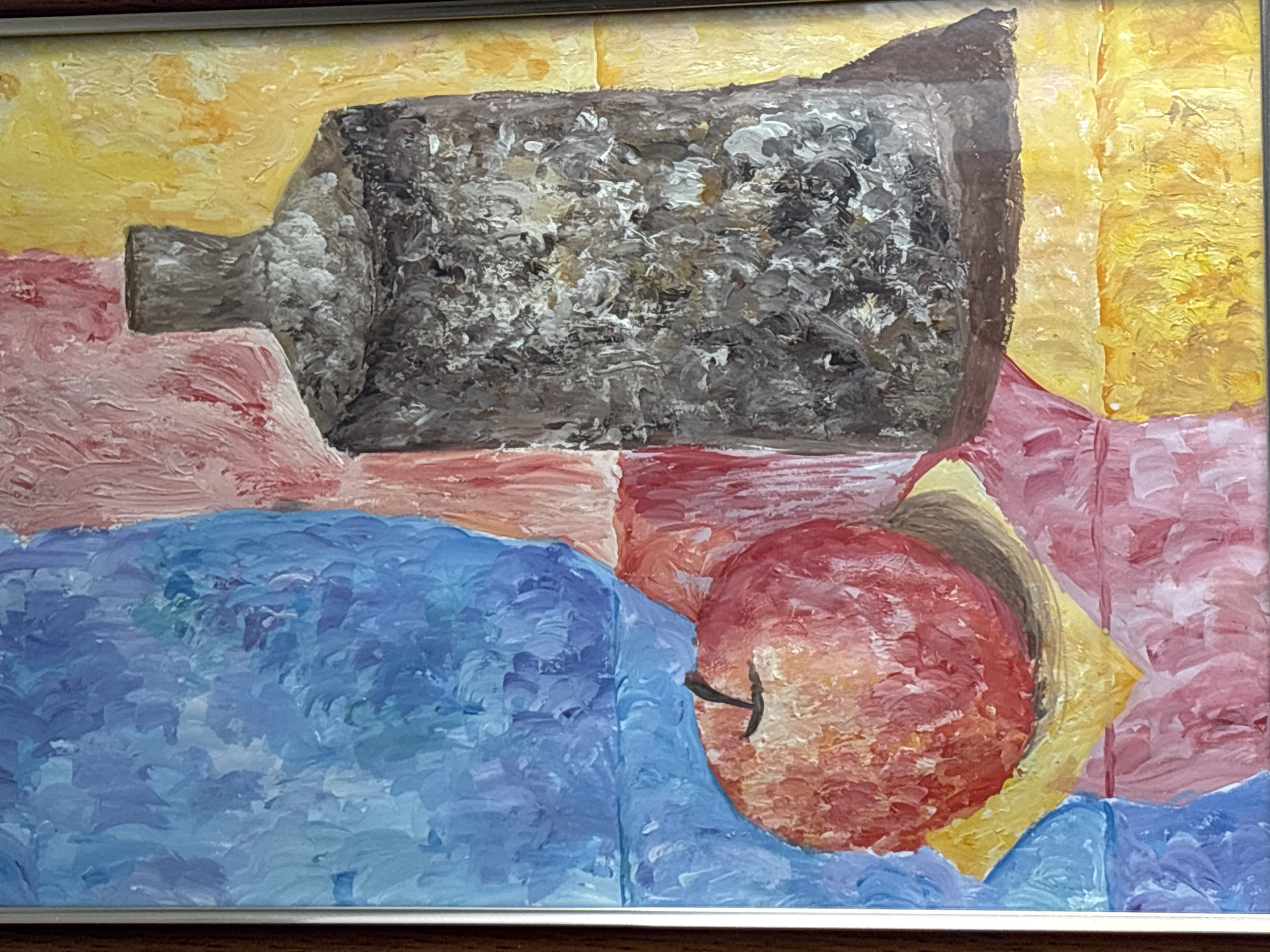 The image is a close-up, framed oil painting. The painting is a still life, featuring an apple and a bottle against a vibrantly colored, abstract background. The apple is rendered in shades of red and orange, with a visible stem. It rests on a yellow surface. To the right of the apple is a dark, textured bottle with a narrow neck and no visible cap. The background is composed of large, vertical strokes of blue, pink, and yellow, creating a sense of abstract drapery or fabric. The painting's textured brushstrokes are clearly visible, suggesting it was painted with thick impasto. There are no people or discernible actions depicted. The image does not contain any visual elements that would allow for the identification of a specific location in the city of Pavlodar, Kazakhstan.