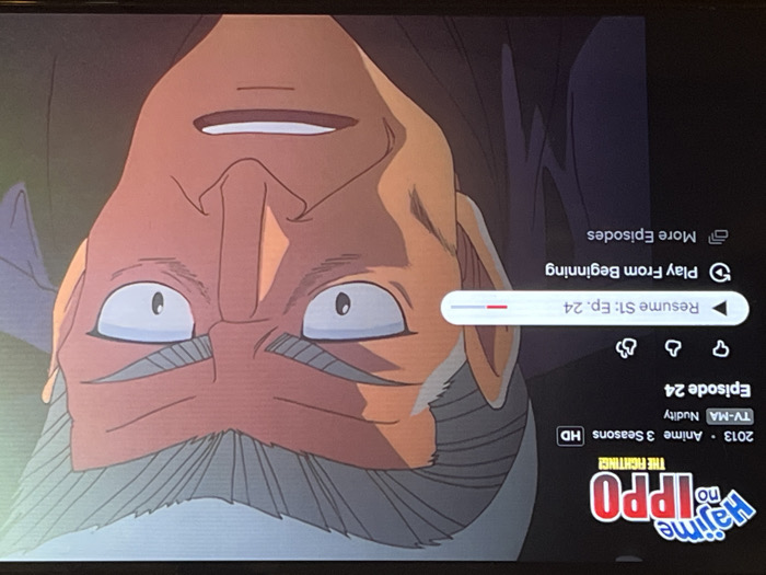 The image displays a screen capture of an anime show streaming on a platform. The title is "Hajime no Ippo: The Fighting!", an anime series from 2013 with 3 seasons in HD. Episode 24 is currently selected and labeled as having nudity. There are options to resume playing from where it left off or to start from the beginning. A cartoonish character with a large mustache is shown in the background, upside down, possibly from the anime series.
