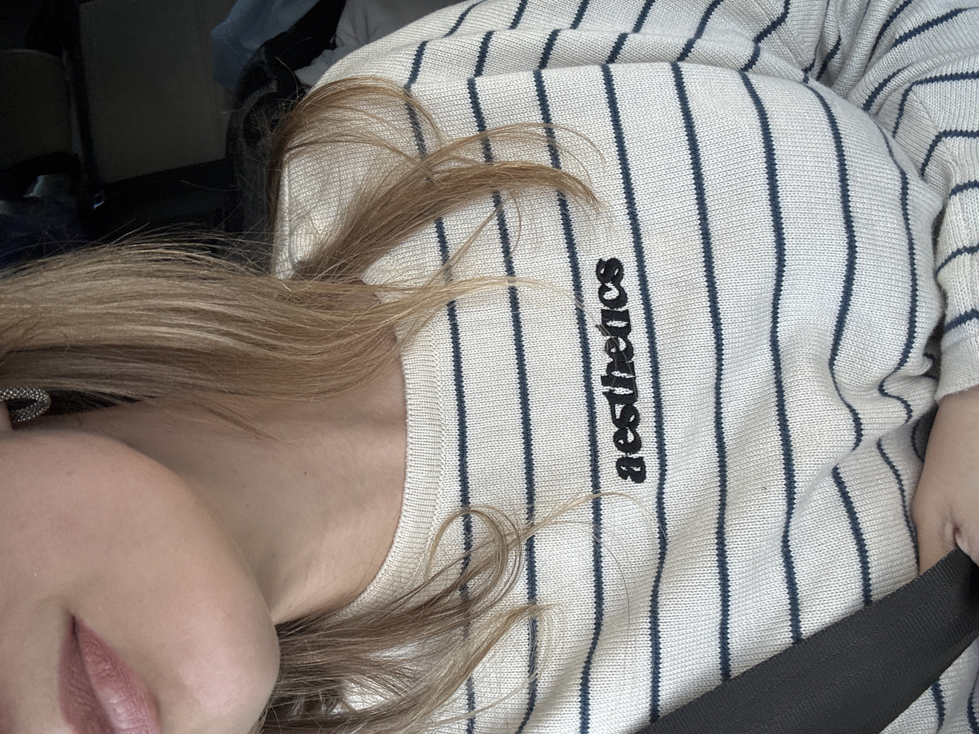 The image shows a person in a vehicle wearing a striped sweater with the word "aesthetics" embroidered vertically. The person is wearing a seatbelt. Part of their face and hair is visible. The background is dark and indistinct, suggesting the inside of a car. The location in Izhevsk, Russia is unknown.