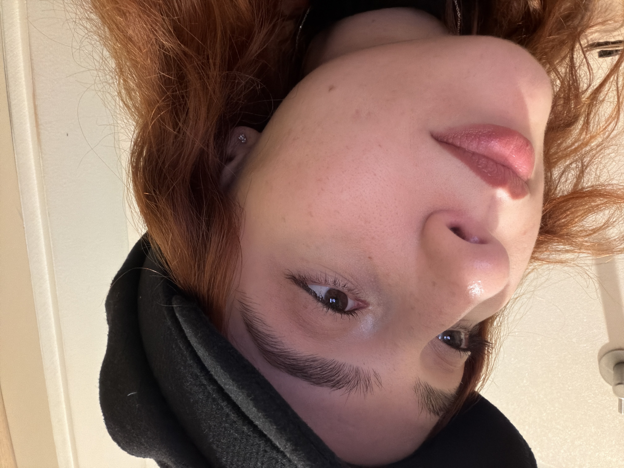A close-up, slightly angled, upside-down view of a person with reddish-brown hair, light skin, and dark eyes. The person is wearing a black garment, possibly a jacket or coat. The background includes a white or light-colored wall and what appears to be a plumbing fixture. There is no discernible information to determine that this image was taken in Strasbourg, France.