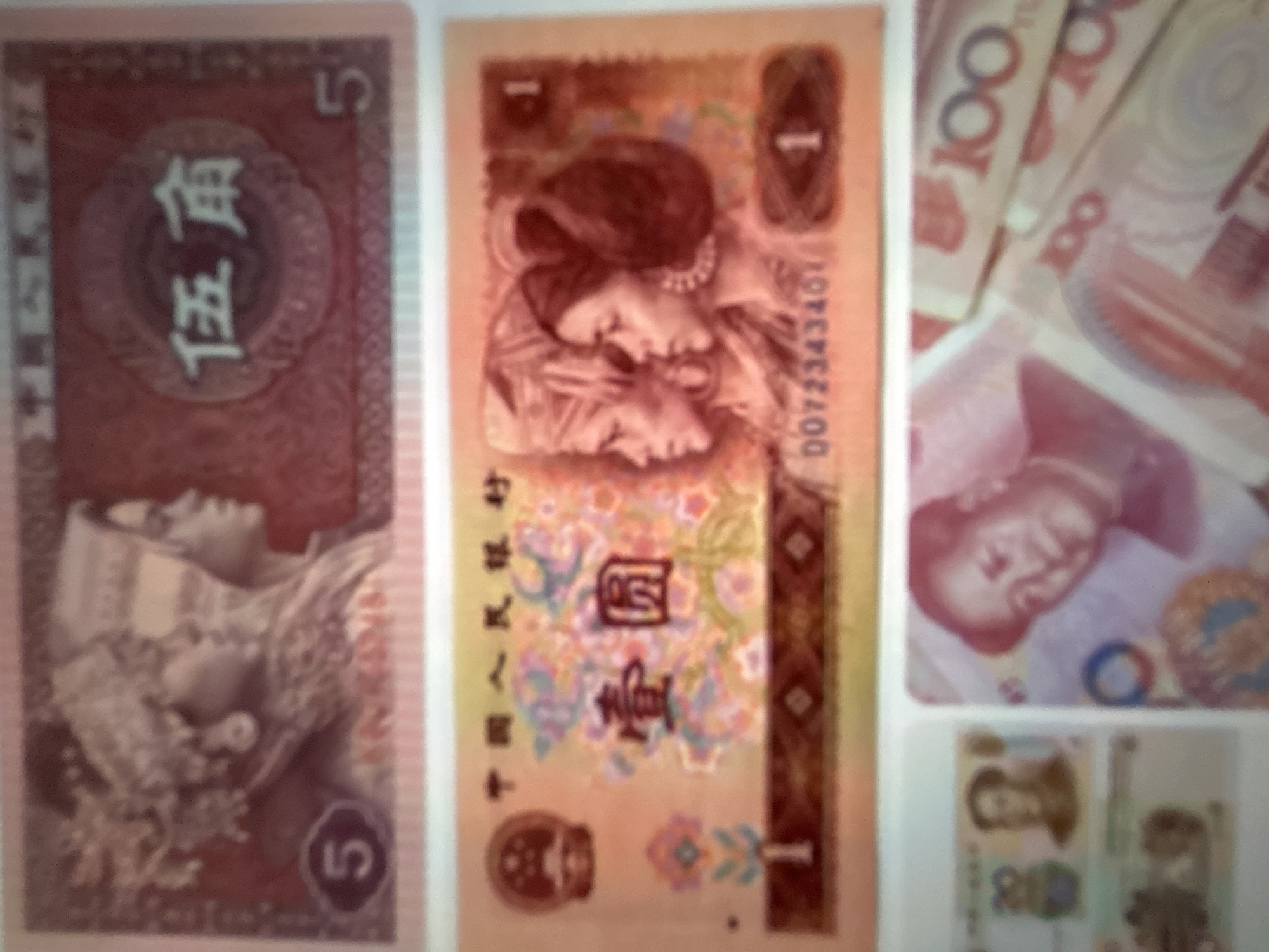 The image displays a collection of Chinese Yuan banknotes. The primary focus is on the banknotes themselves, with no discernible scene, setting, or activity beyond the presentation of the currency.
On the far left, a red banknote is visible, featuring the Chinese characters "伍角" (Wǔ jiǎo), meaning "five jiao," and a numeral "5". A stylized image of what appears to be a person in traditional attire is also present.
The central banknote is a light orange color and features two faces in profile, one superimposed on the other, and the numeral "1". To the right of these faces, a serial number "DO72343461" is visible. Vertical text in Chinese characters is present on the left side of this banknote, and a large Chinese character that appears to be "圓" (yuán), meaning "yuan," is prominently displayed in the center.
To the right of the central banknote, several red and white 100 Yuan banknotes are fanned out, with the numeral "100" clearly visible on each. Below these, a portion of another banknote is visible, featuring a portrait of a person.
The bottom portion of the image shows smaller banknotes, with one appearing to be a 1 Yuan note with a portrait and the numeral "1". Another smaller note, possibly a 5 Yuan note, is also partially visible.
There are no indicators of time of day, weather, or specific emotions conveyed by the images. The context of Gelendzhik, Russia, is provided but is not visually represented within the image itself. The overall impression is a display of Chinese currency, likely for informational or illustrative purposes.