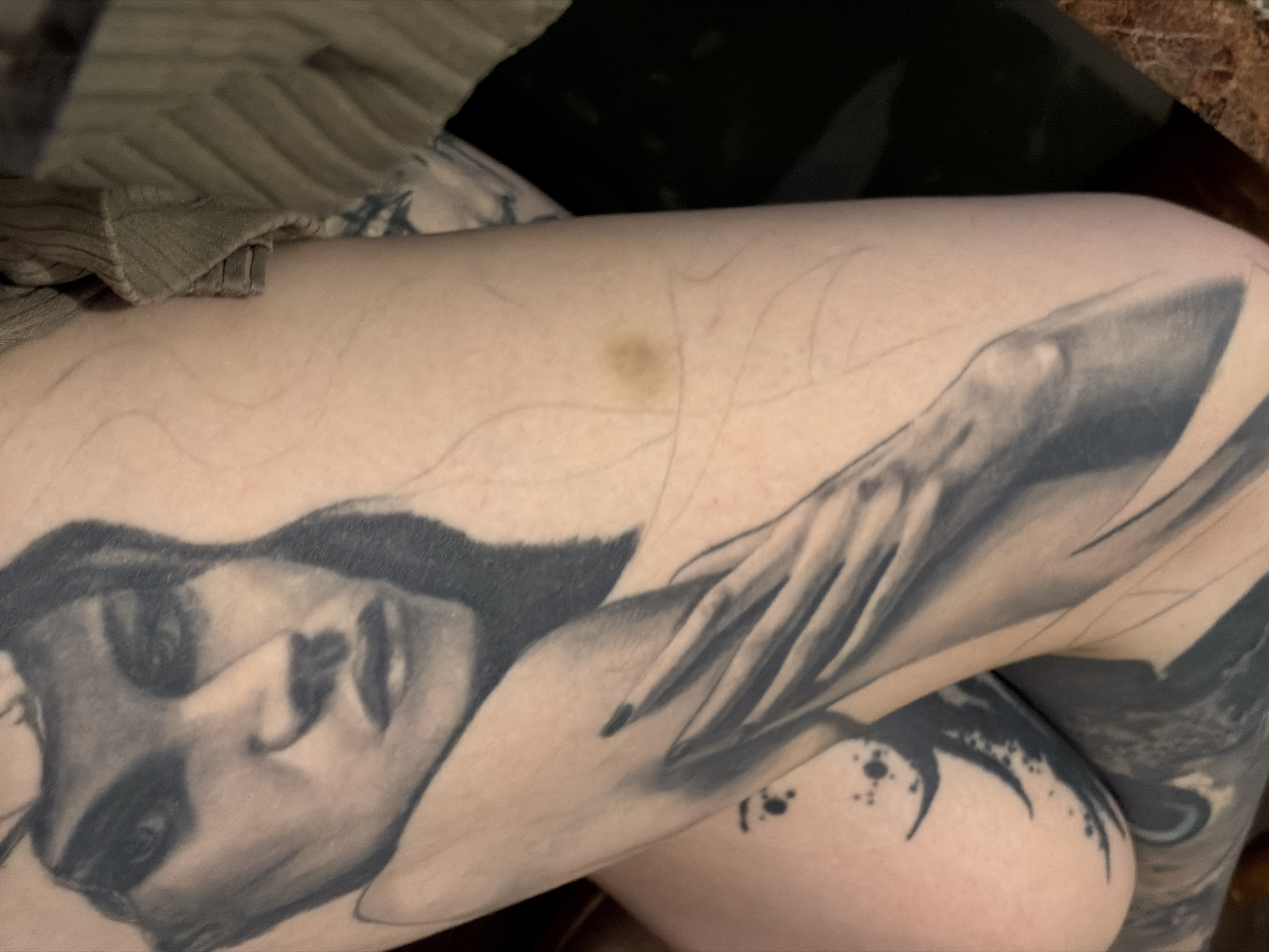 A close-up photograph depicts a person's tattooed thigh and knee. The tattoo features a woman's face and a hand with long, pointed fingers. A small bruise is visible on the thigh above the tattoo. The setting is not explicitly identified, so determining the location in Chaikovsky, Russia, is not possible without further information.