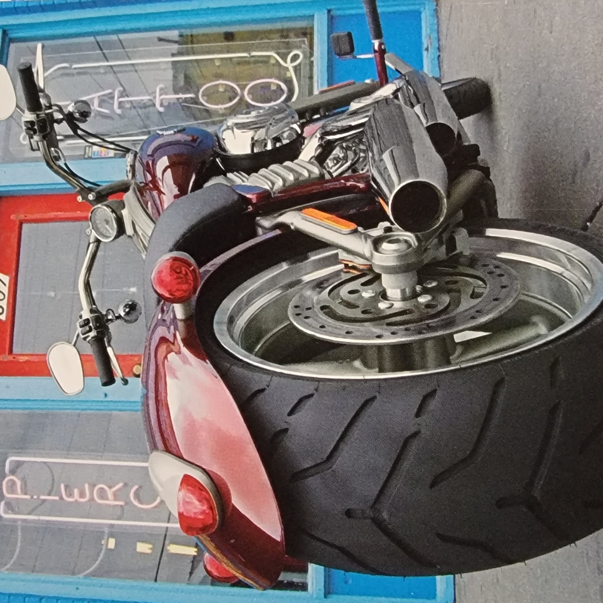 A low-angle, full shot depicts the rear side of a red motorcycle parked outside a building. The motorcycle is the primary subject, with its large rear tire and chrome accents prominently featured. Behind the motorcycle, the building's facade is visible, characterized by a bright blue frame around a red door. Neon signs are attached to the building; one on the left reads "PIERC" in white cursive letters stacked vertically, and another on the right has vertical white lettering that appears to spell "TATTOO". The ground is paved with concrete. There are no people visible in the image.