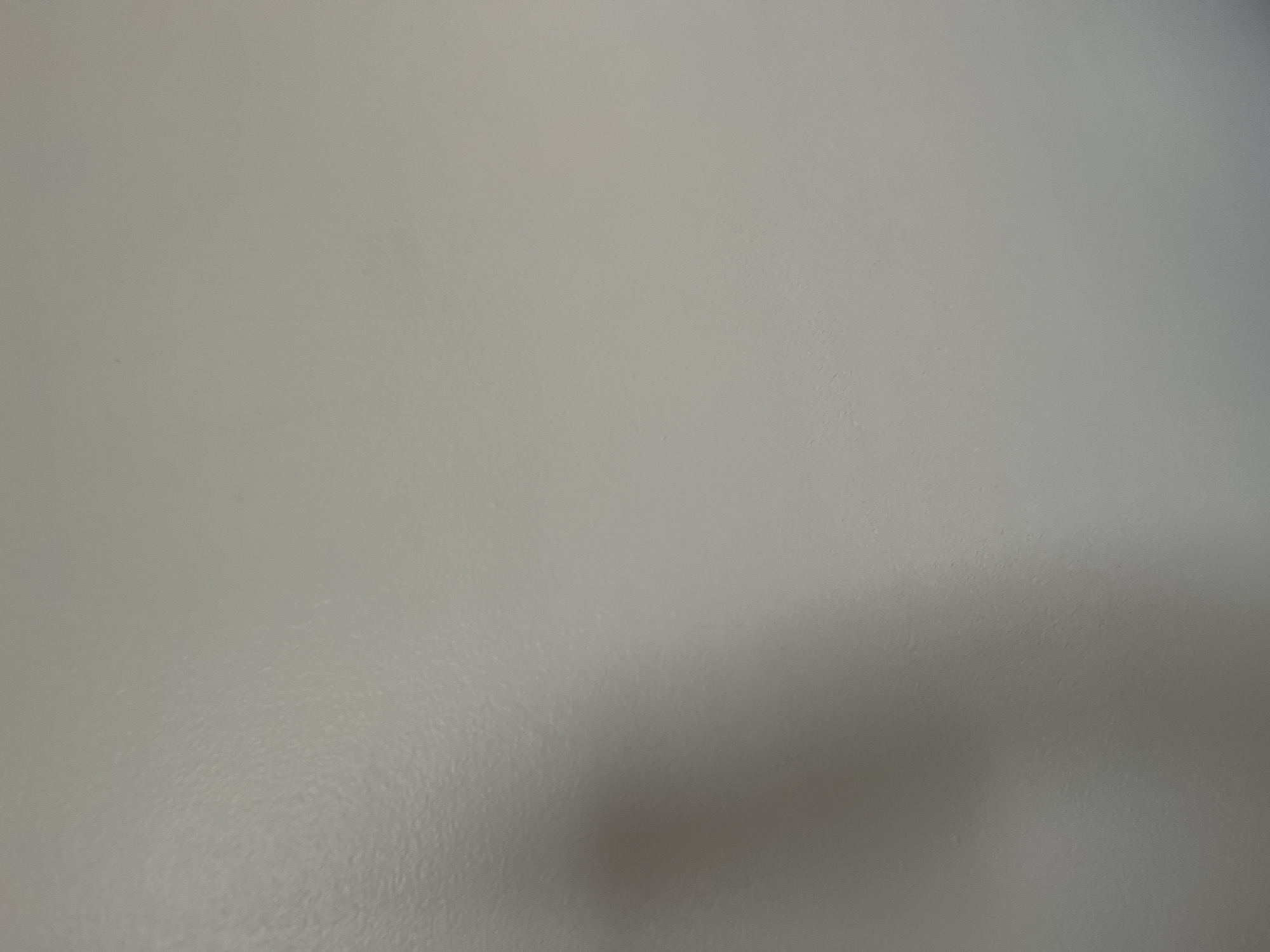 A soft shadow, possibly of a person's head and shoulder, is visible on a light gray painted wall. The wall has a slightly textured, matte finish. The shadow is cast from the left side of the image and tapers off towards the center and right. There are no other discernible objects or people in the frame. The scene appears to be an indoor wall. The location within West Hartford, United States of America, cannot be determined from the visual information provided.