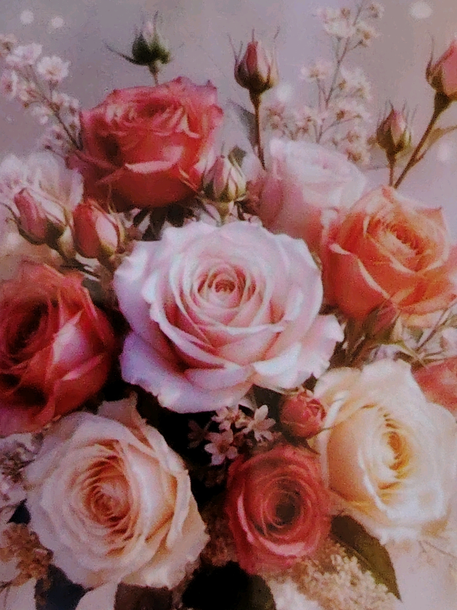 The image is a close-up, top-down shot of a bouquet of roses. The roses are of varying colors, including pink, red, and cream. Some roses are fully bloomed, while others are still buds. The bouquet is arranged with delicate filler flowers and greenery. The background is softly blurred, suggesting a shallow depth of field. The overall impression is one of delicate beauty and natural elegance. There are no people or specific landmarks visible in the image, and therefore no connection to Mazyr, Belarus can be made.