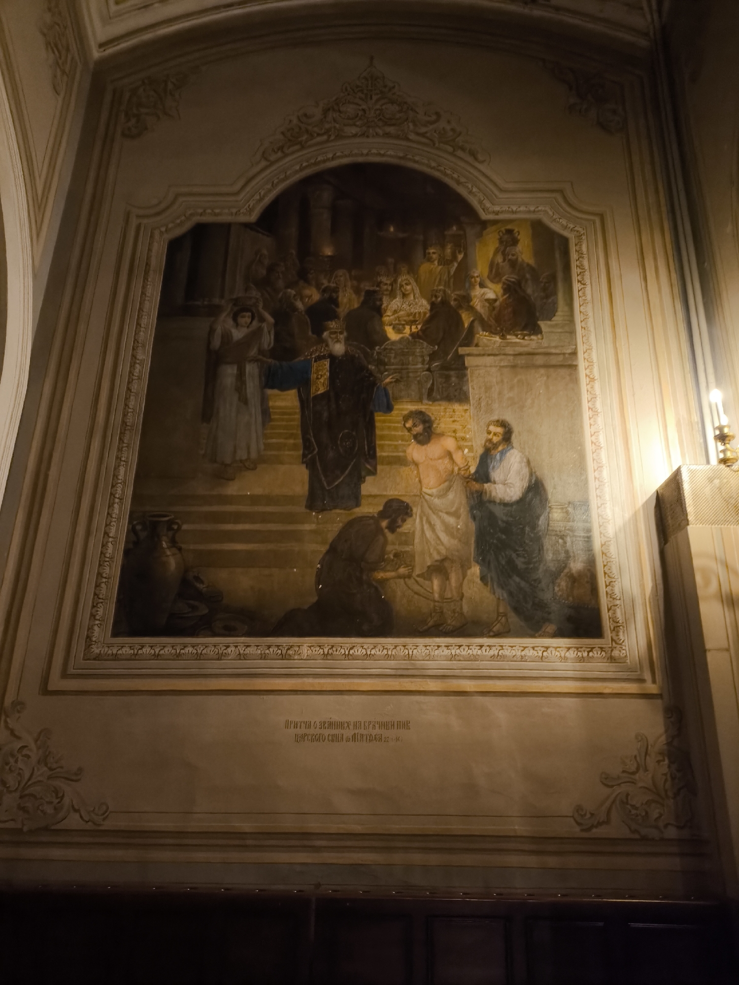 Captured within an ornate, arch-framed recess on a wall is a classical-style painting depicting a religious scene. Figures ascend steps; an old man in dark robes gestures downwards towards two semi-nude individuals, with one kneeling. Behind them, another man stands with a draped robe. At the top of the steps, a crowd of figures stands, including one holding a golden crown. Below the painting, faintly visible text is inscribed on the wall. The painting is situated in an interior space, illuminated by a candle in the corner to the right. The location is in the city of Unknown, Unknown.