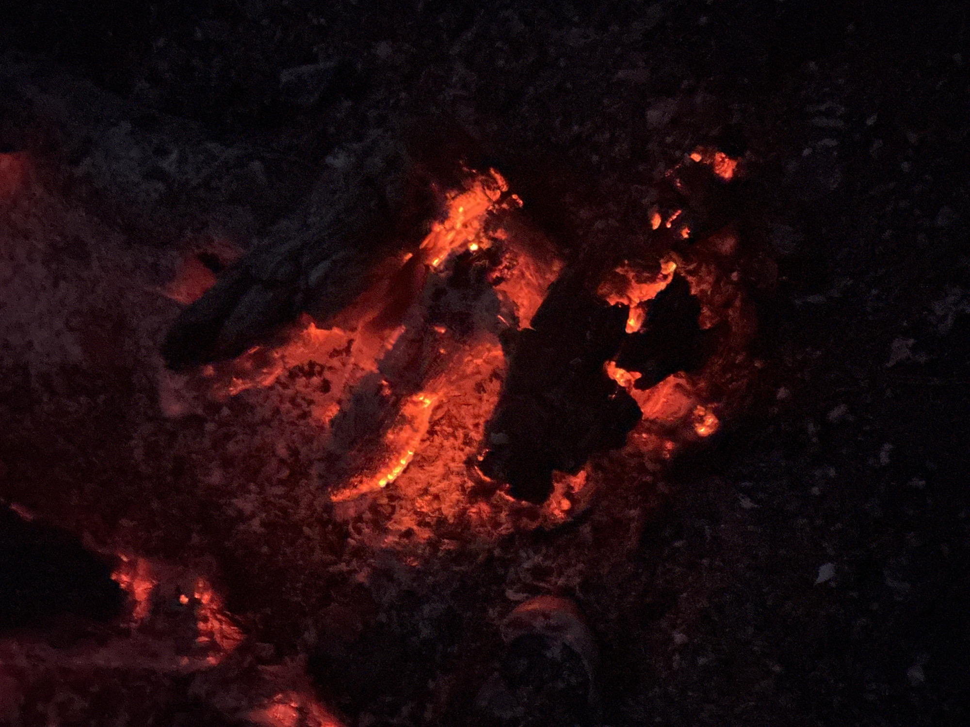 The image depicts a close-up view of burning embers and ash, suggesting the aftermath of a fire. The predominant color is red, radiating from the active embers. The surrounding area appears dark and charred. The location in Папярнянскі сельскі Савет, Belarus is not discernible from the image. There are no people, subjects, objects or actions that indicate the location.