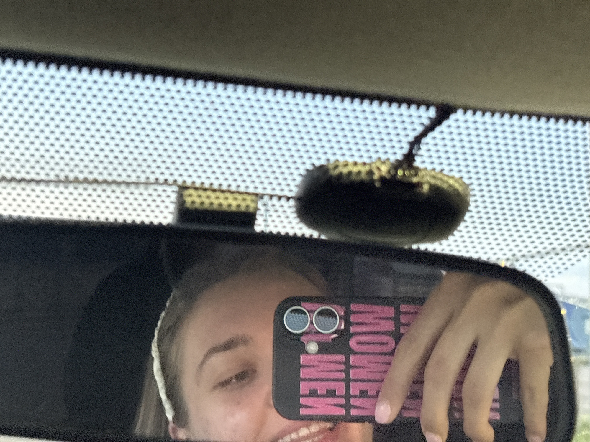 A woman takes a selfie in the rearview mirror of a vehicle. The phone case says "Money Moves". The location is likely within a vehicle but the scene is not discernable to be in Perm, Russia.
