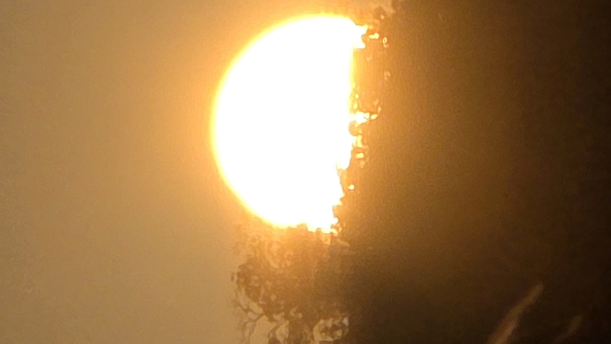 A hazy, distorted view of the sun, partially obscured by a dark, indistinct foreground. The image has a monochromatic, golden-brown cast. The edges of the sun appear irregular. No identifiable location in Bac Natural Heritage Area Trang, Vietnam can be discerned. There are no people or identifiable objects.